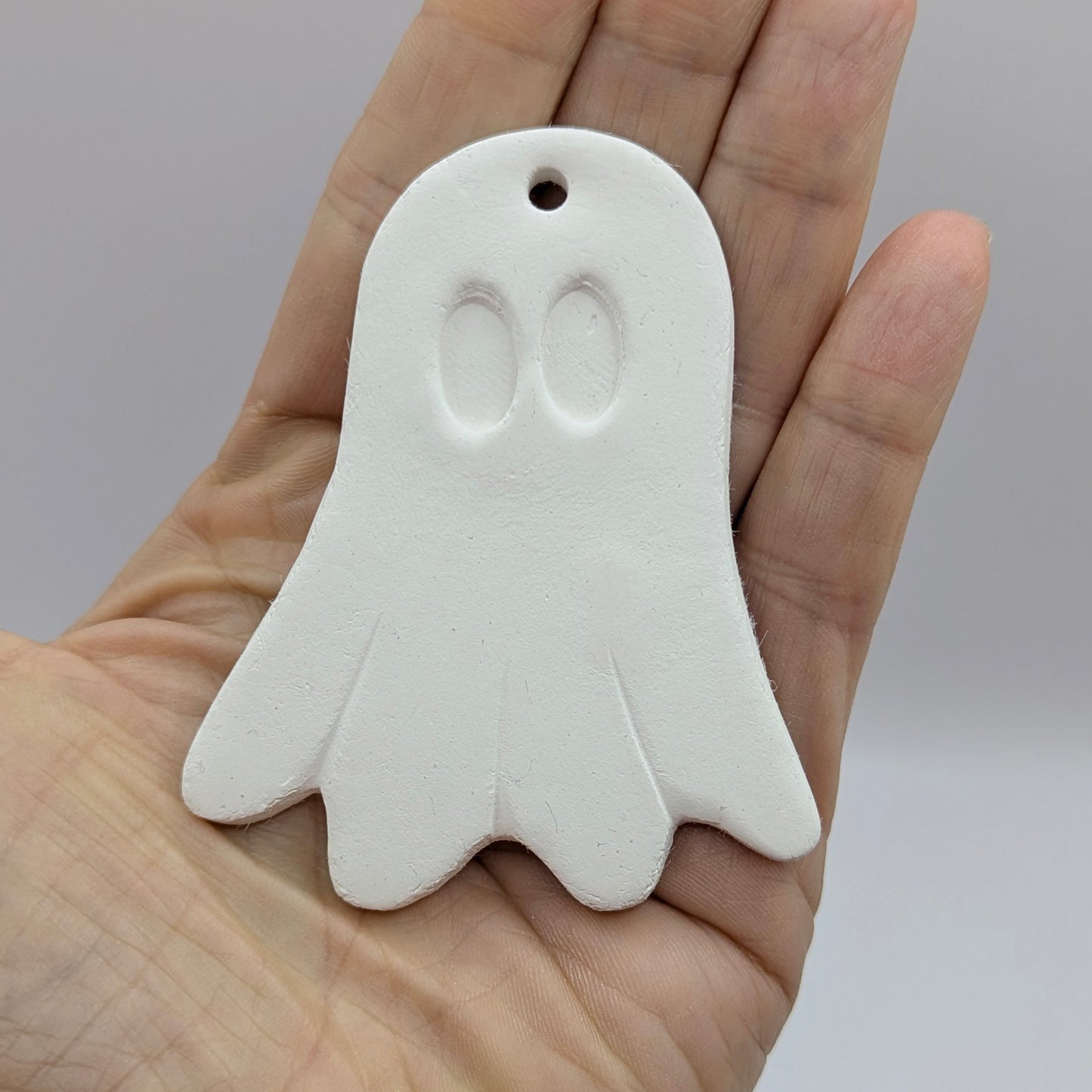 White ghost-shaped decoration held in a hand against a neutral background