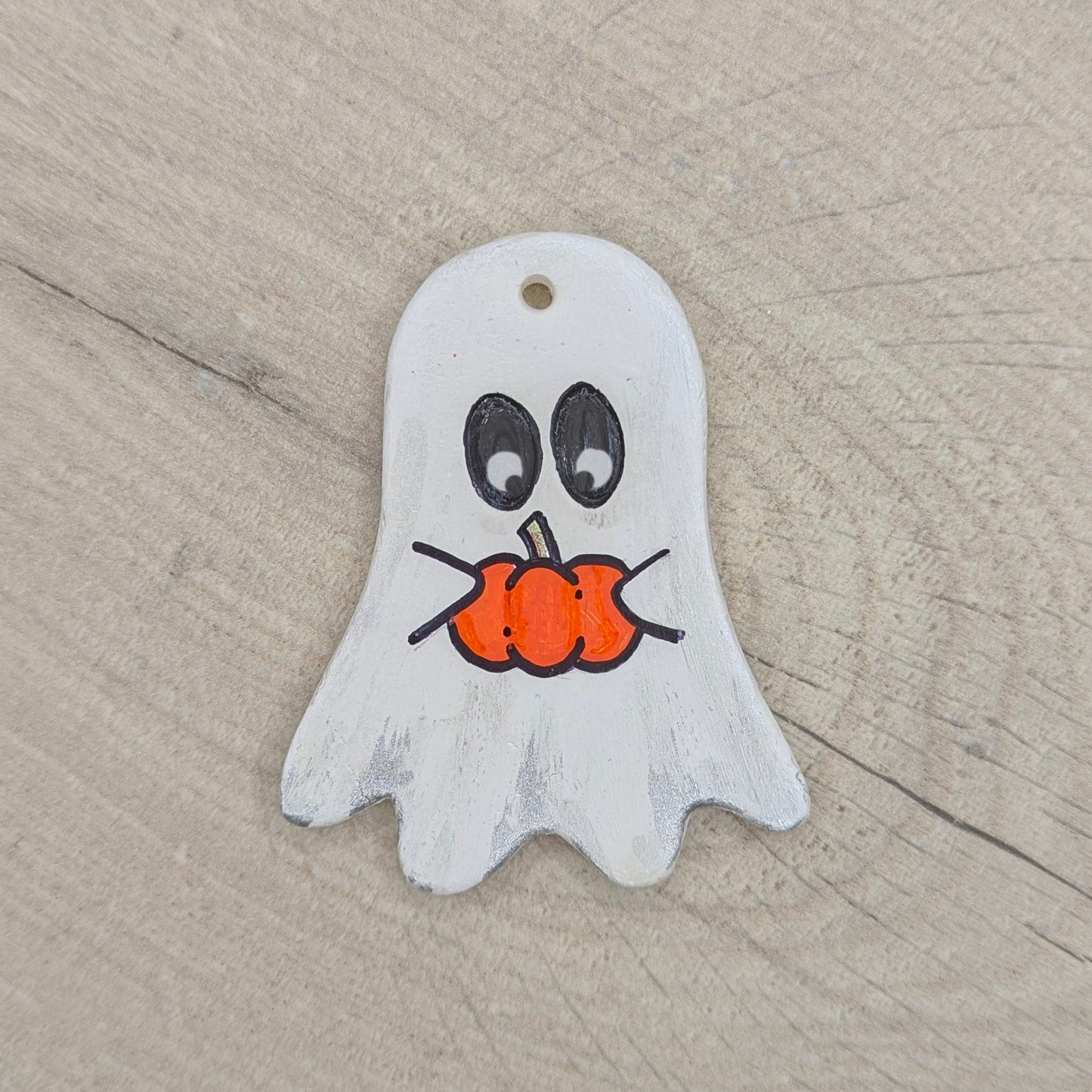Ghost-shaped clay decoration holding a pumpkin on a wooden surface