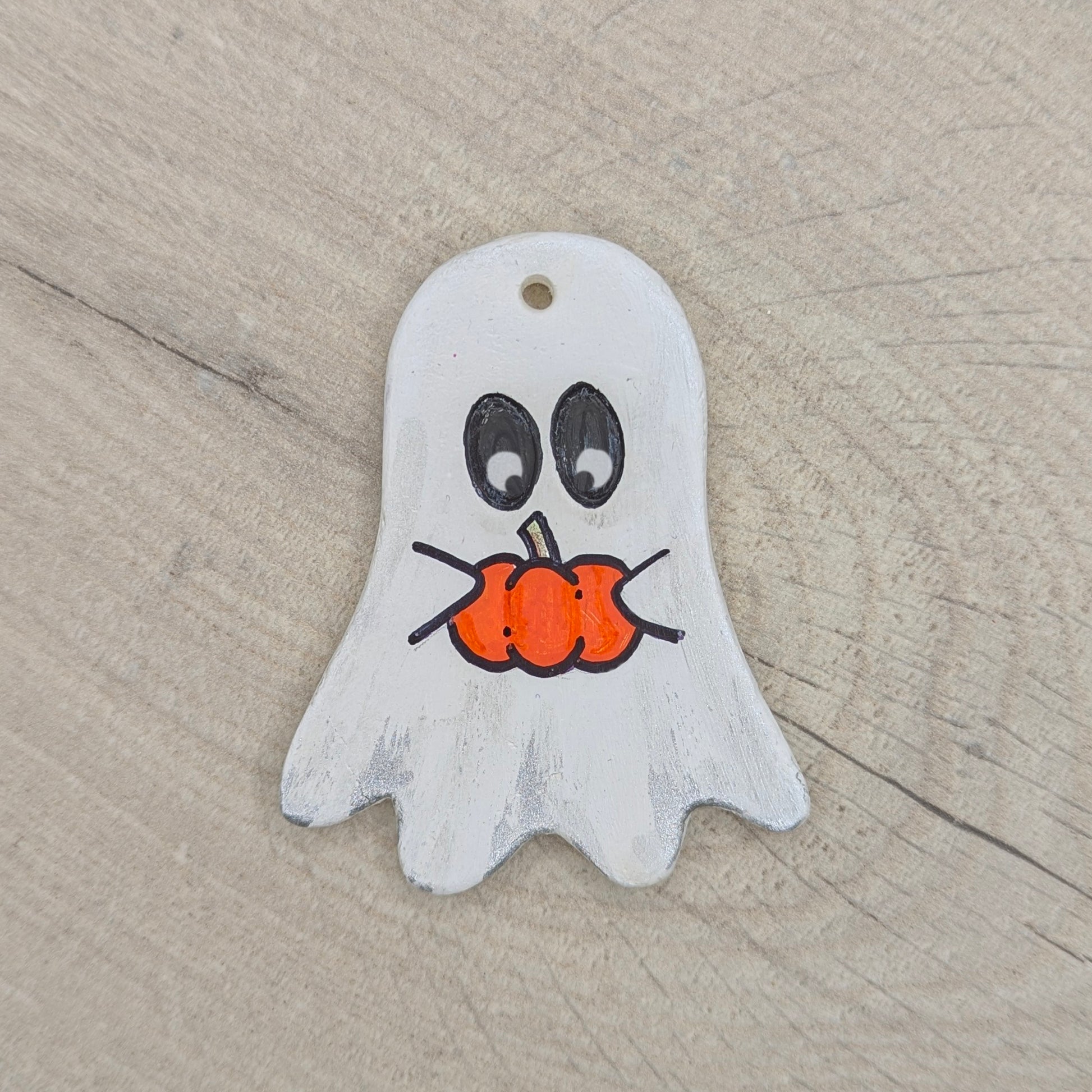 Ghost-shaped clay decoration holding a pumpkin on a wooden surface