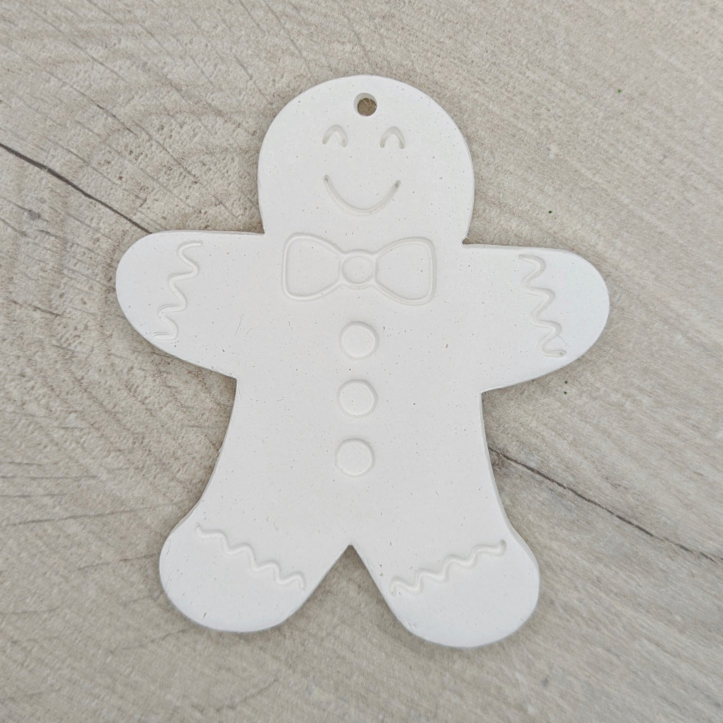 White clay gingerbread man ornament, with a eyes, mouth, bow tie and buttons stamped into the clay, on a wooden surface