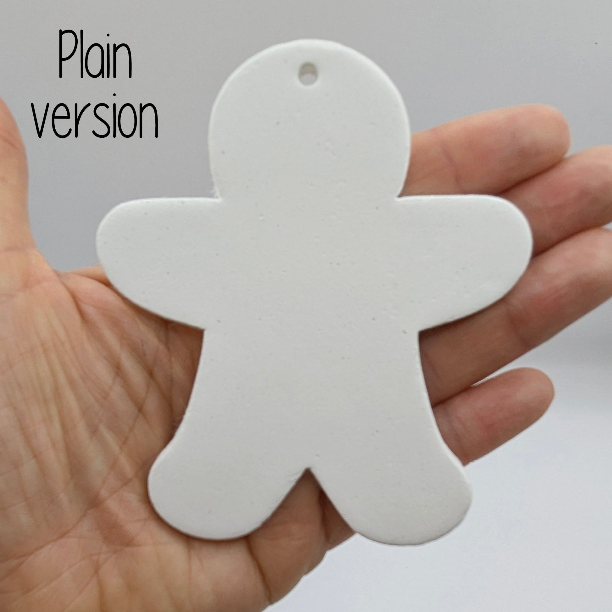 Plain white clay gingerbread man shaped ornament held in a hand against a grayish background