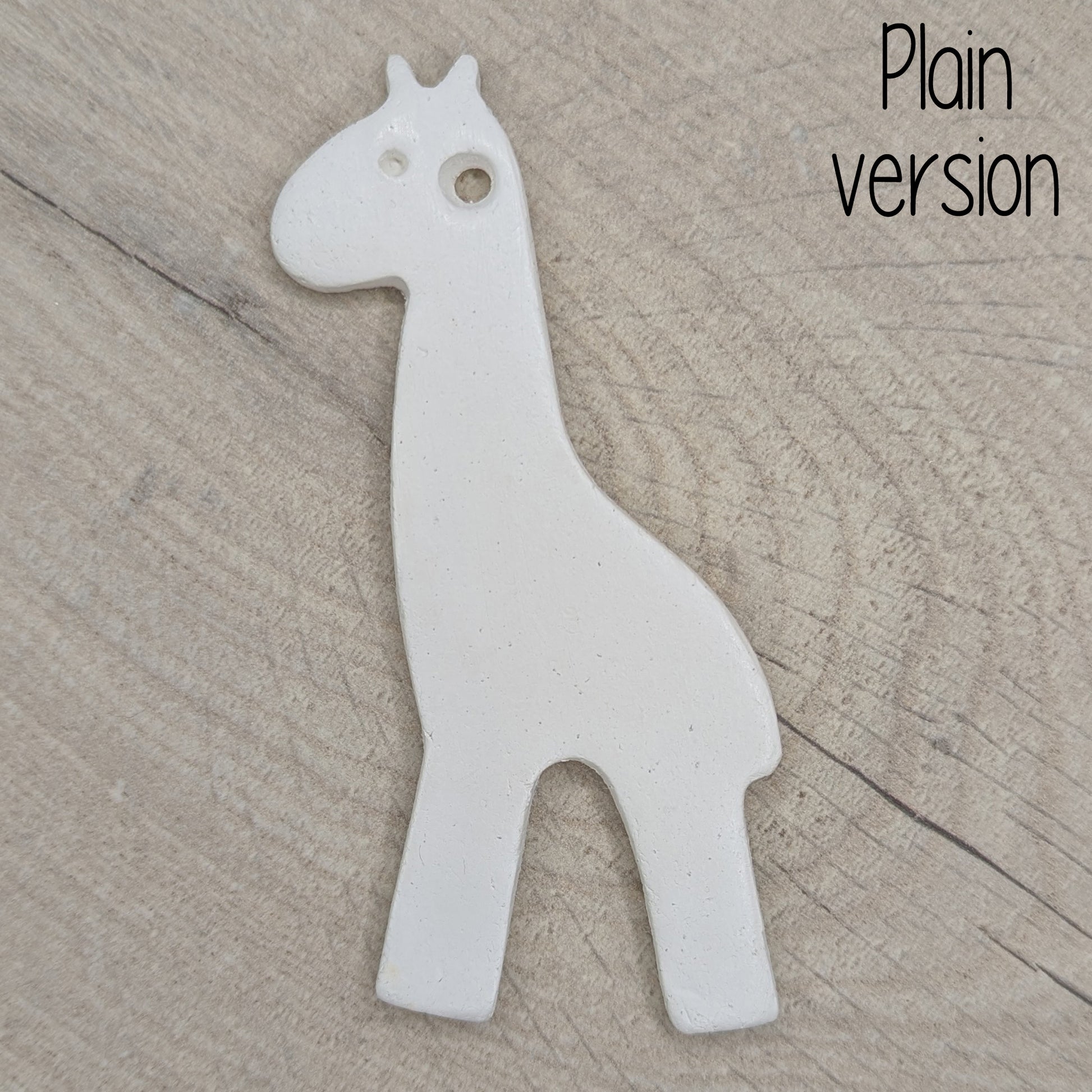 White giraffe shaped clay decoration on a wooden surface, plain version other than an eye stamped in