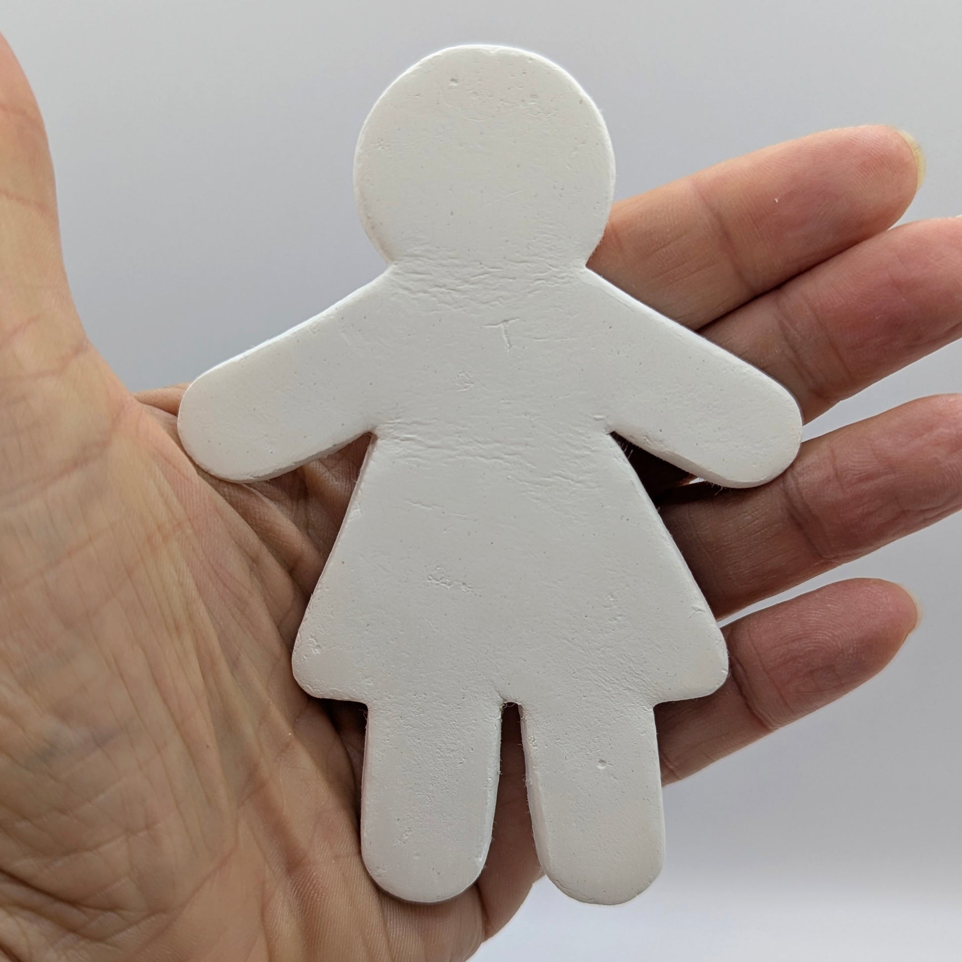 Hand holding a white clay female shaped figure against a plain background