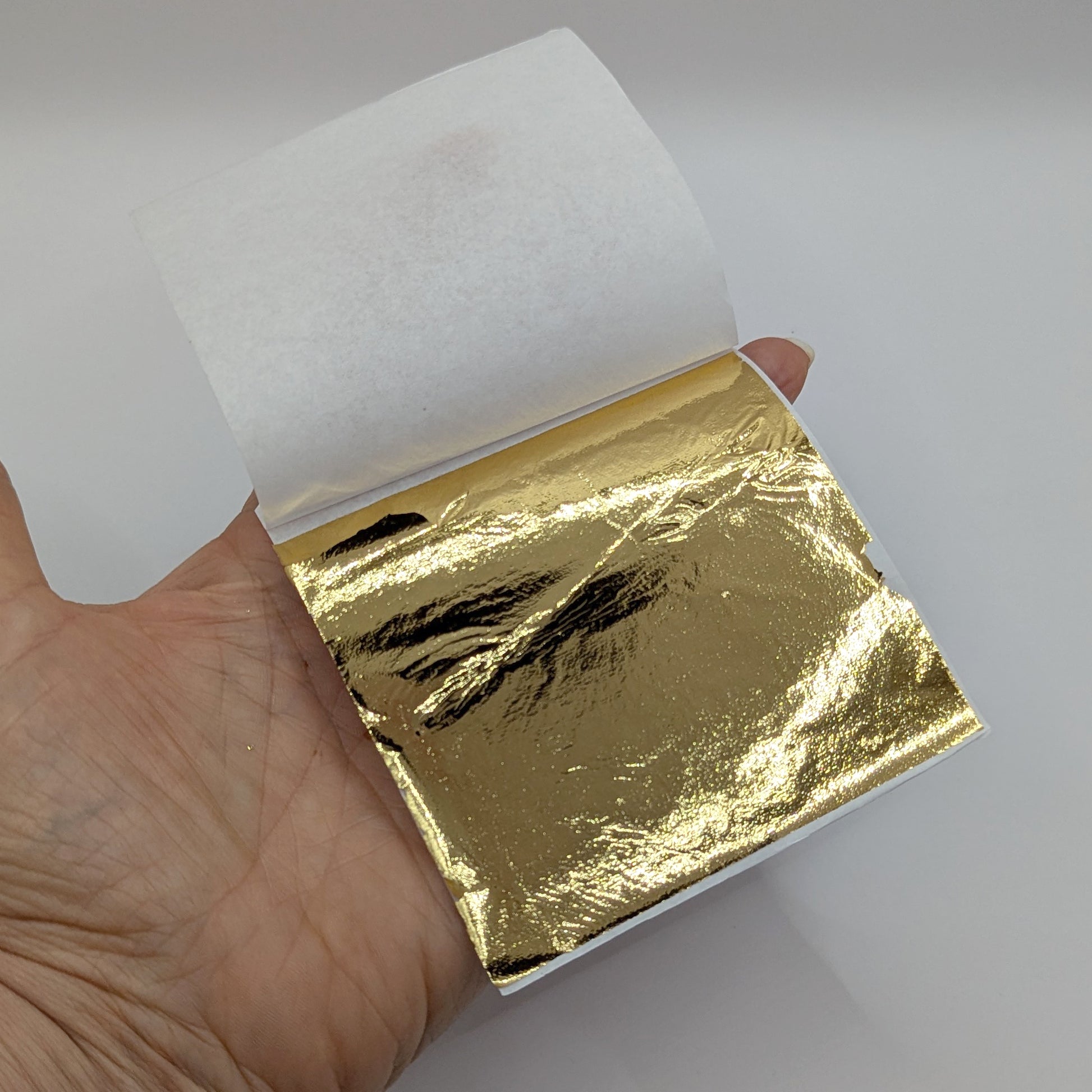 Hand holding a book of gold leaf pages against a white background