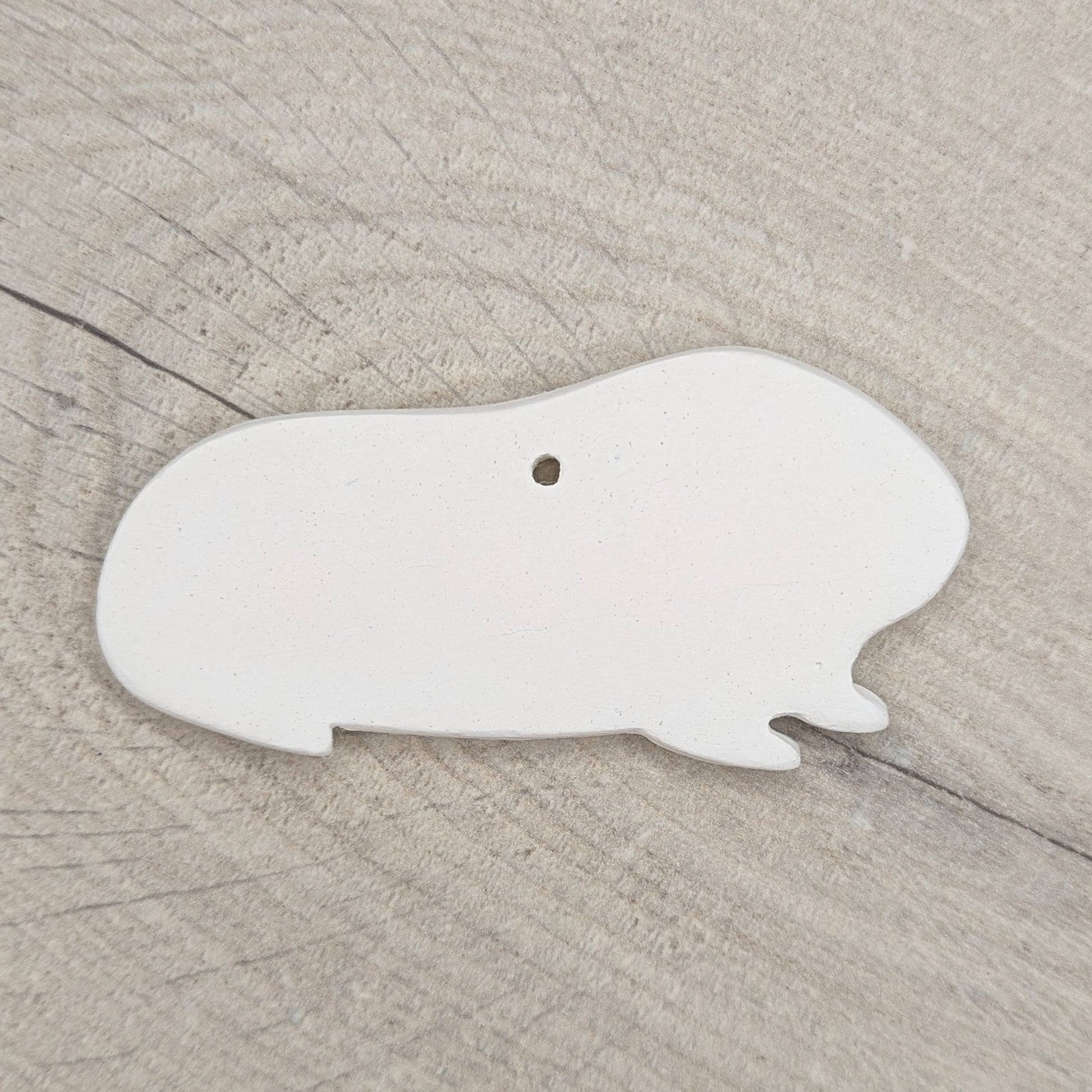 white air dried clay guinea pig shaped decoration on wooden background to paint at home