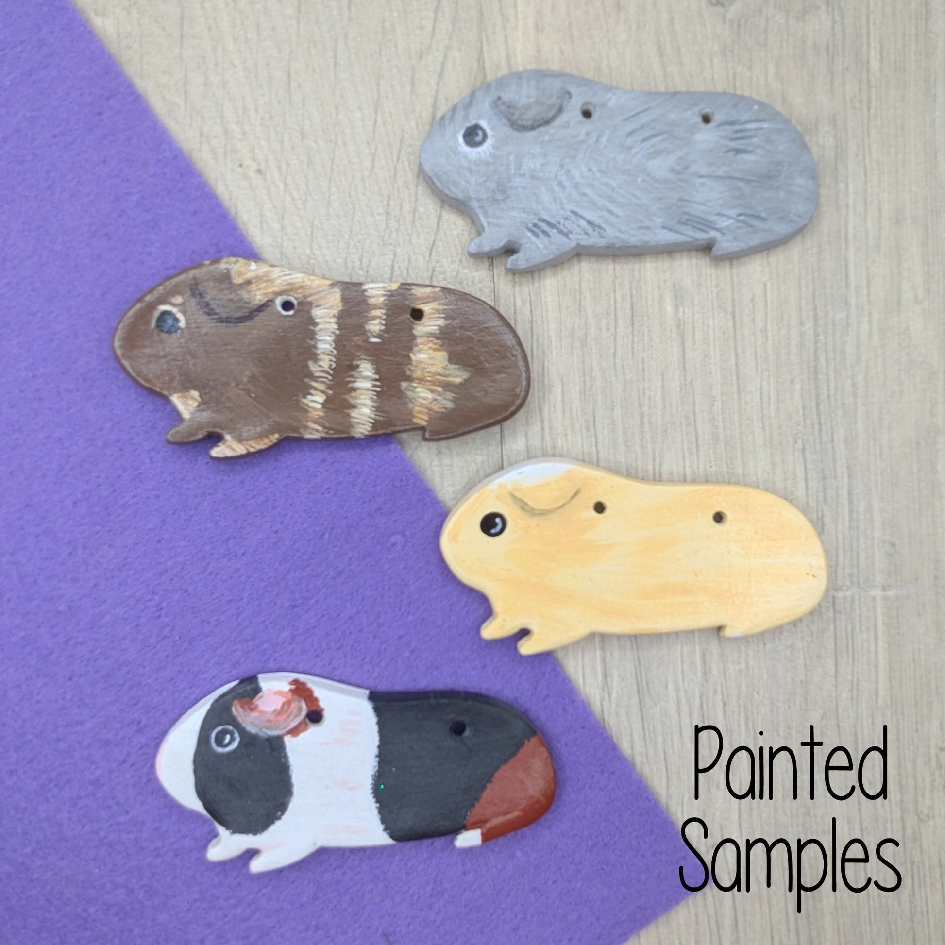 selection of different coloured / painted guinea pig clay decorations, one Agouti grey, one brown, one fawn and the last one a tri coloured white, black and brown