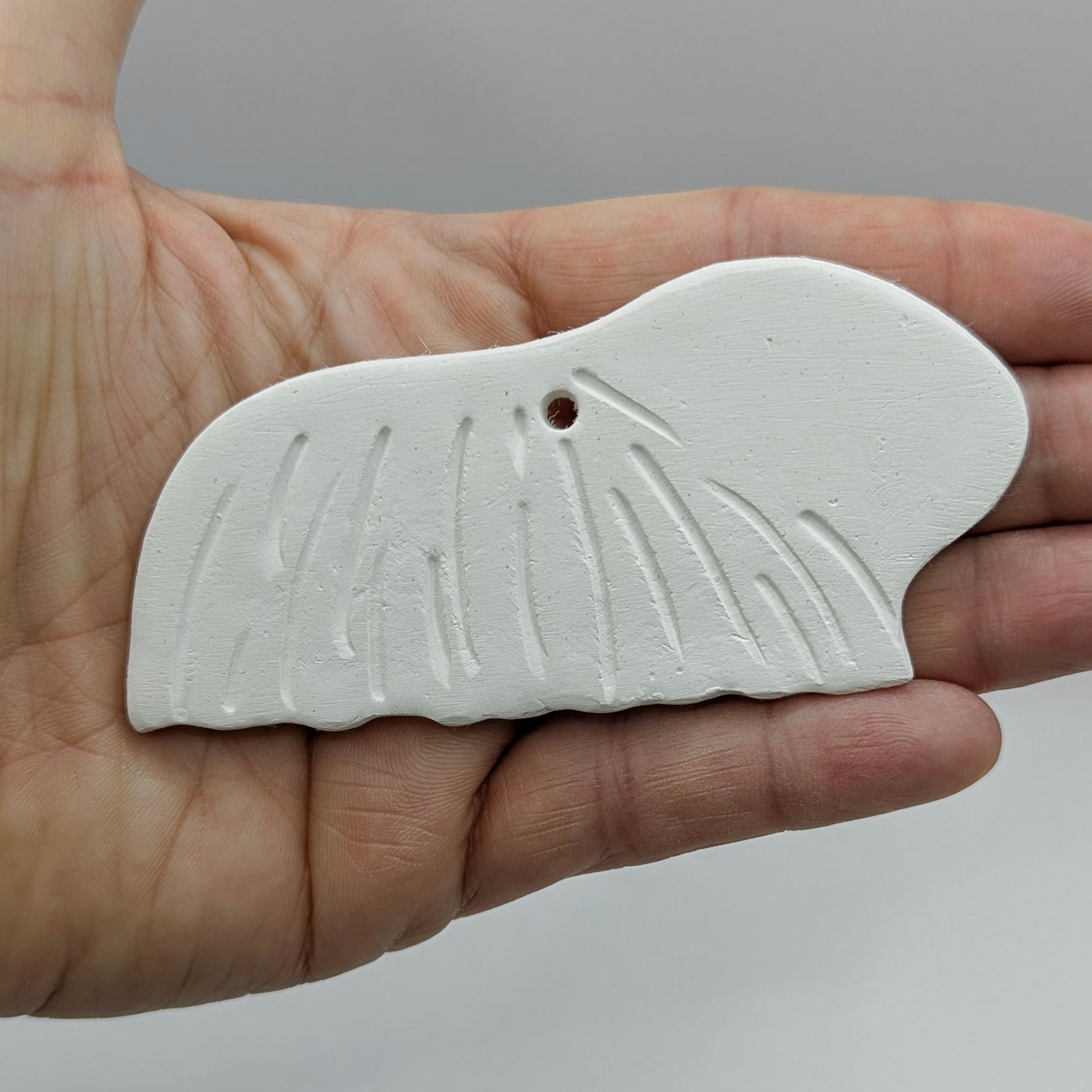 long haired guinea pig clay decoration, held in a hand on a grey background