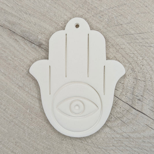 White Hamsa hand clay decoration with eye symbol on a wooden surface