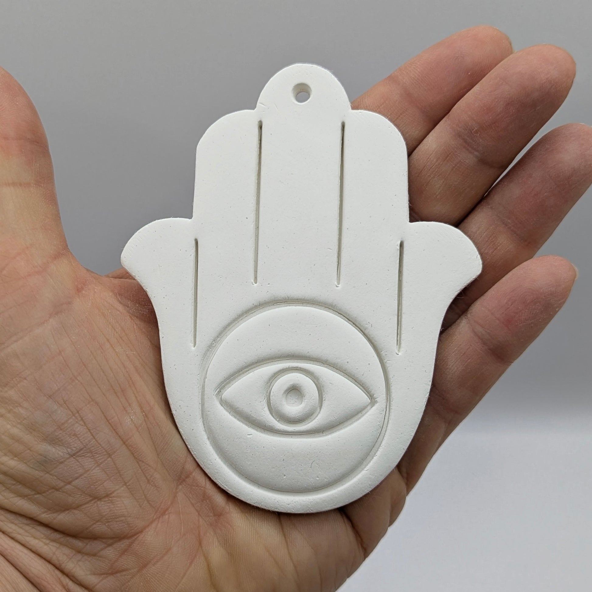 White Hamsa hand with eye design held in a hand against a gray background