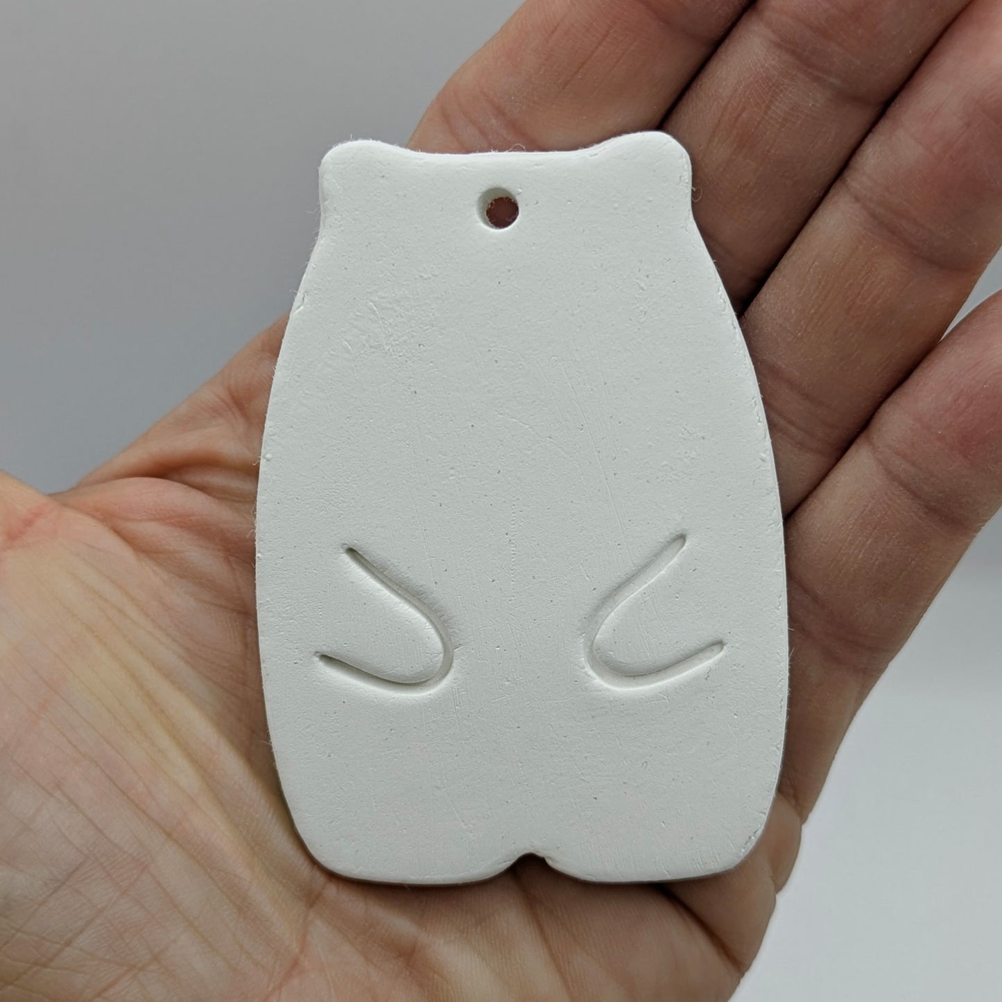 White clay hamster shaped decoration held in a hand against a neutral background