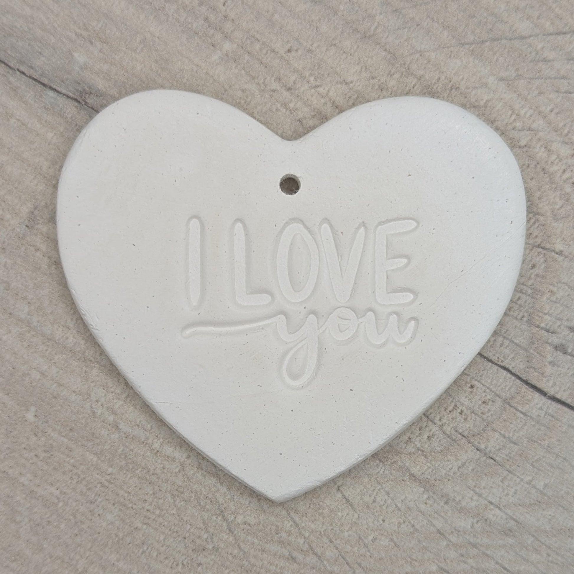 Heart shaped air dried clay decoration / tag with 'I LOVE YOU' stamped into the clay, on wooden background