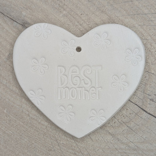 Heart shaped air dried clay decoration / tag with 'Best mother' and small flowers stamped into the clay, on a wooden surface