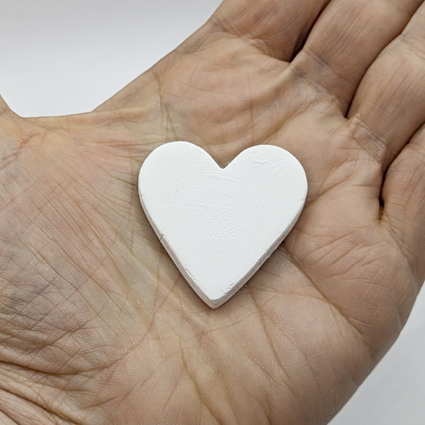 White heart shaped clay decoration held in a hand 