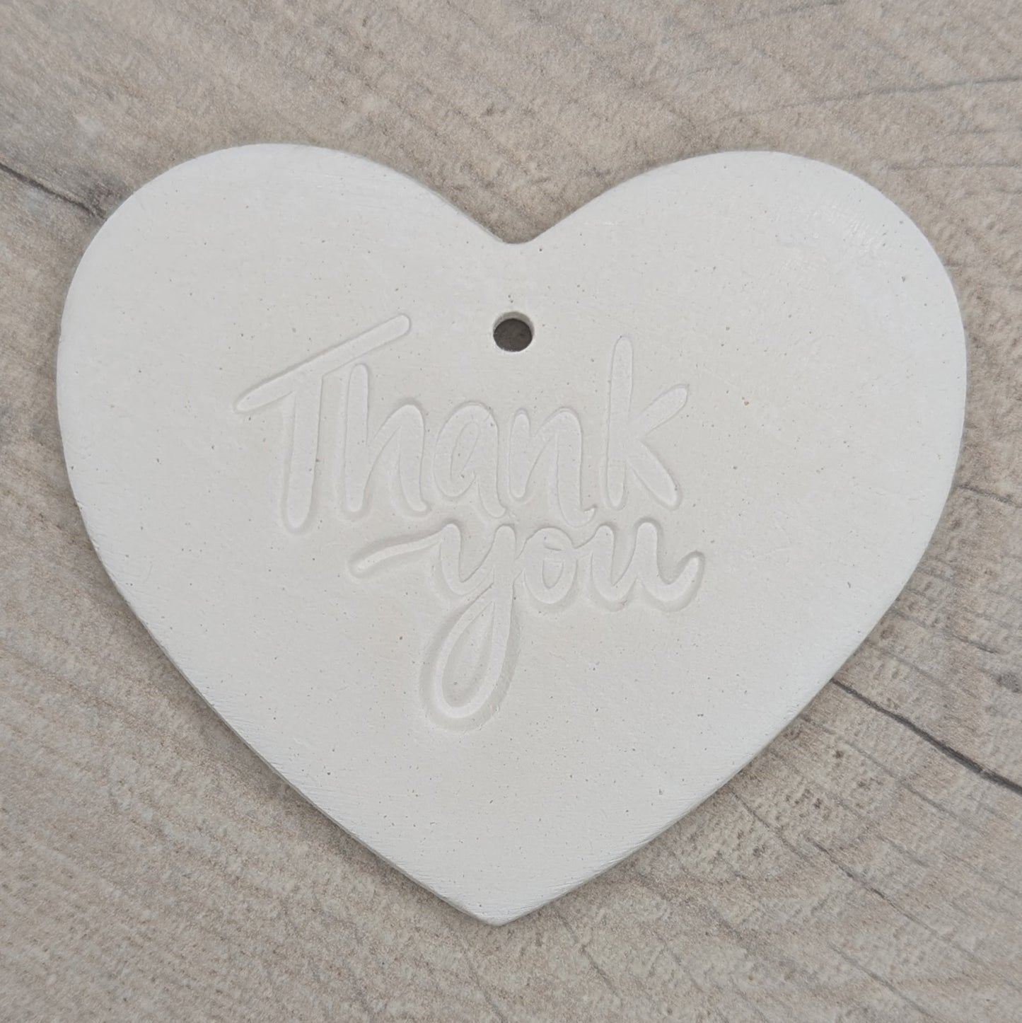 Heart shaped air dried clay decoration / tag with 'thank you ' stamped into the clay, on a wooden background