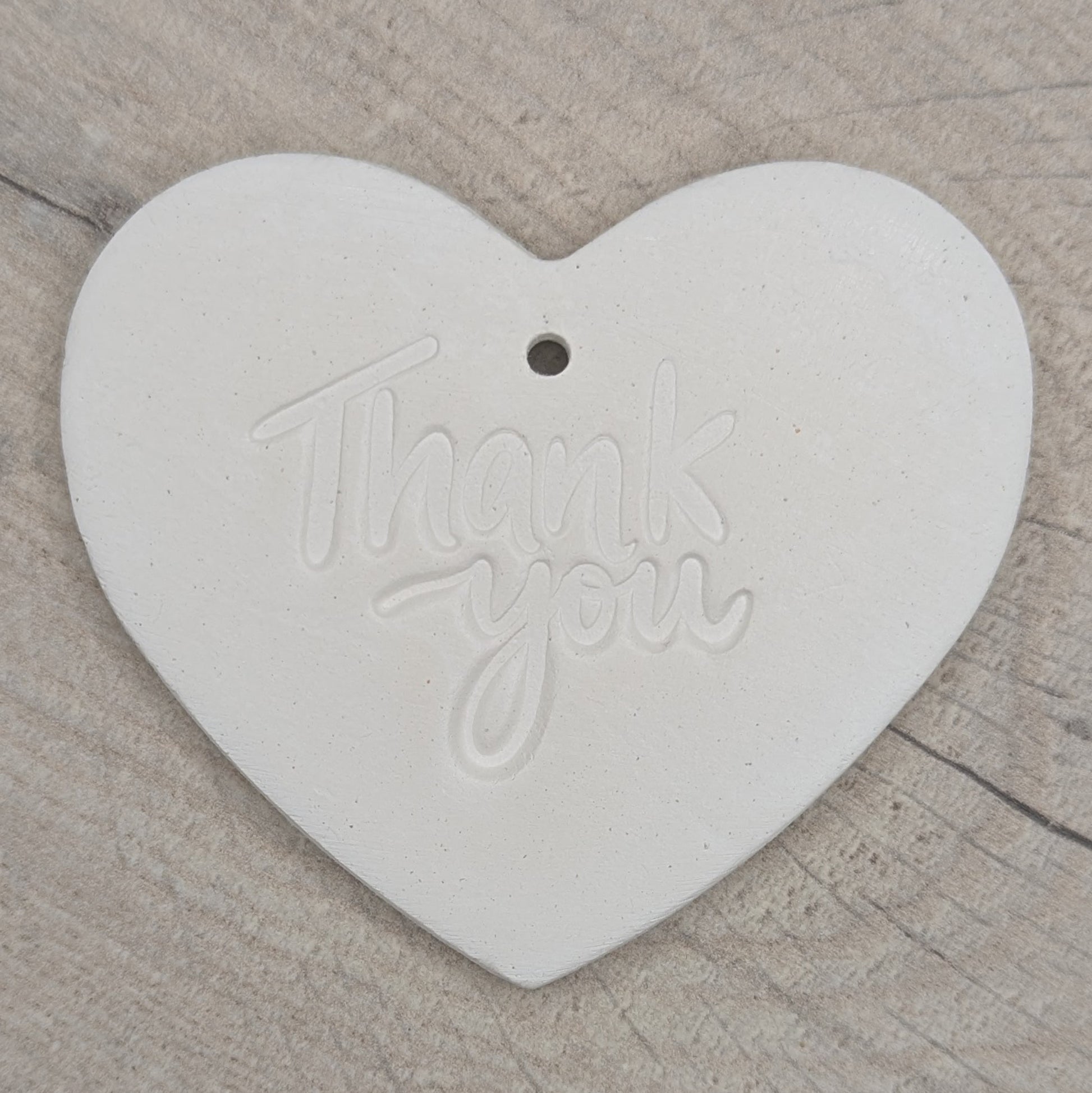 Heart shaped air dried clay decoration / tag with 'thank you ' stamped into the clay, on a wooden background