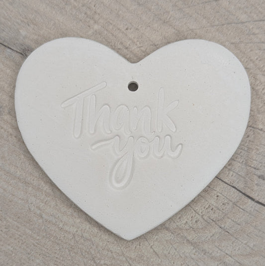 Heart shaped air dried clay decoration / tag with 'thank you ' stamped into the clay, on a wooden background