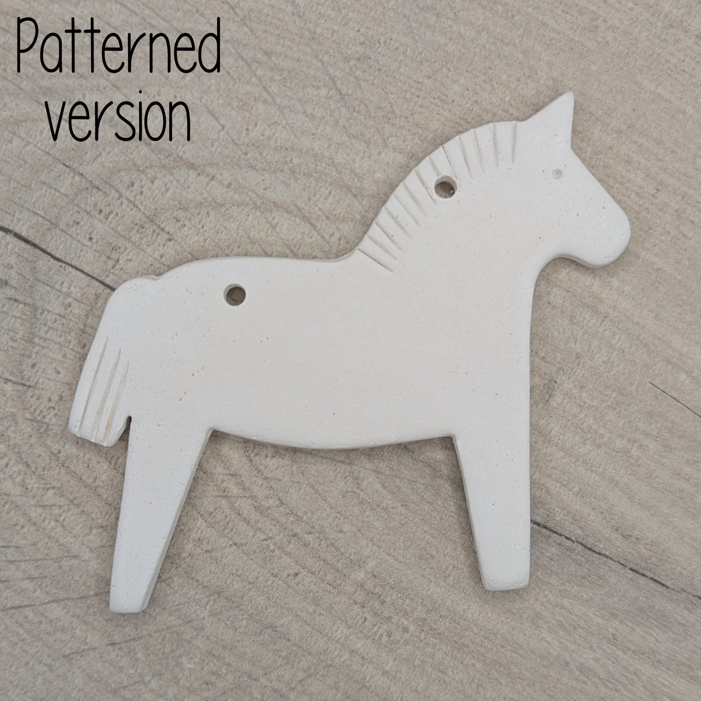 Horse shaped white clay decoration  on a wooden surface, pattern on mane and tail