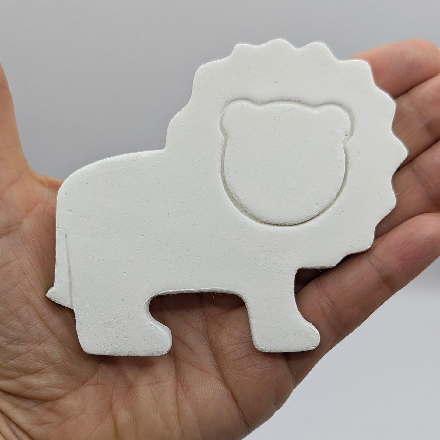 White lion-shaped decoration held in a hand against a gray background
