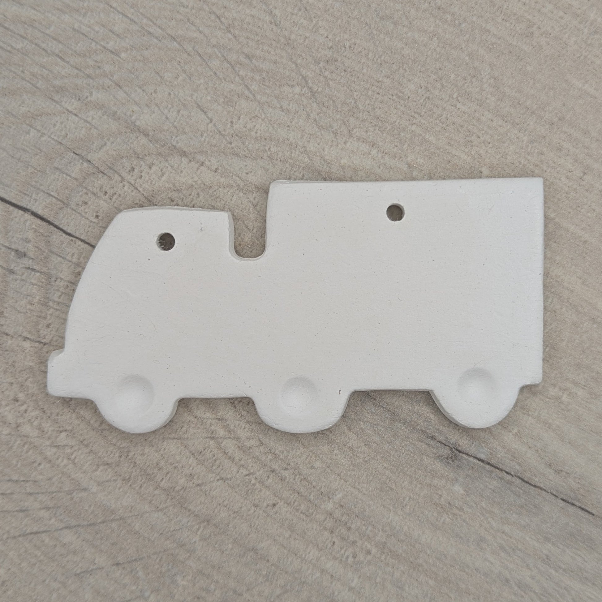 White clay lorry decoration with wheels stamped into the clay, on wooden background