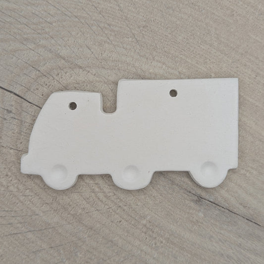 White clay lorry decoration with wheels stamped into the clay, on wooden background