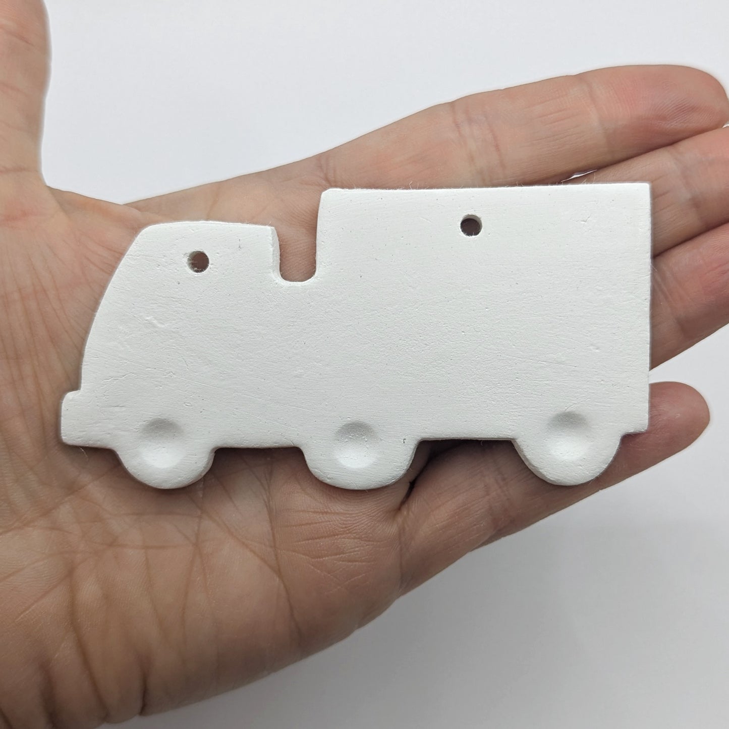 White clay lorry decoration with wheels stamped into the clay, held in some ones hand for scale