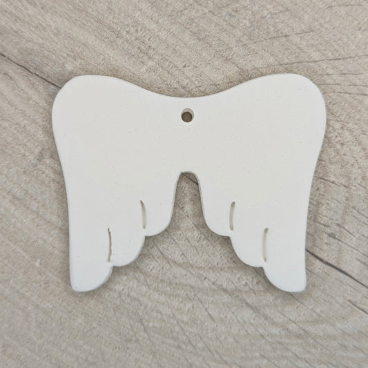 white air dried clay memorial angel wings, shown on a light wood background