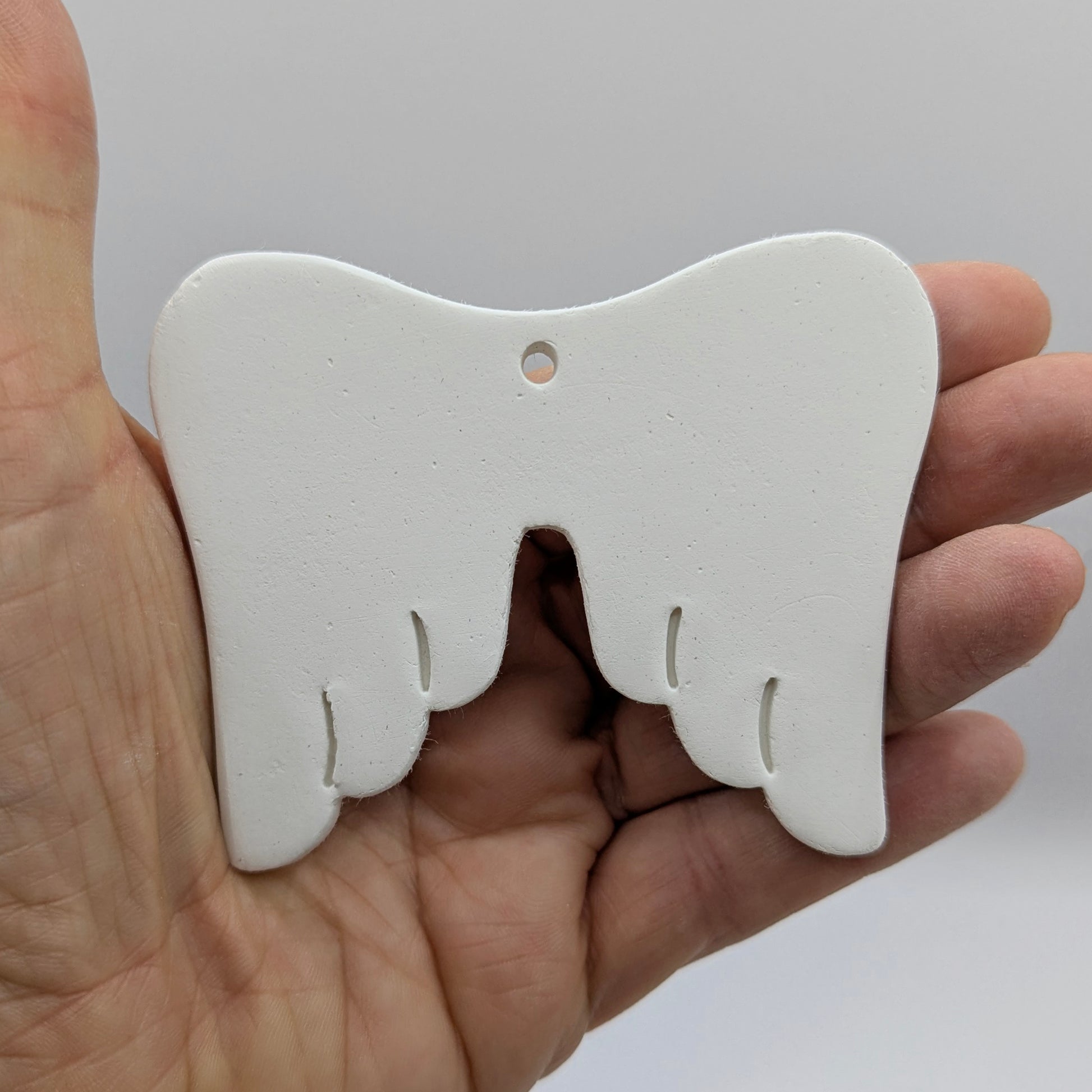 white air dried clay memorial angel wings, shown in some ones hand to show scale