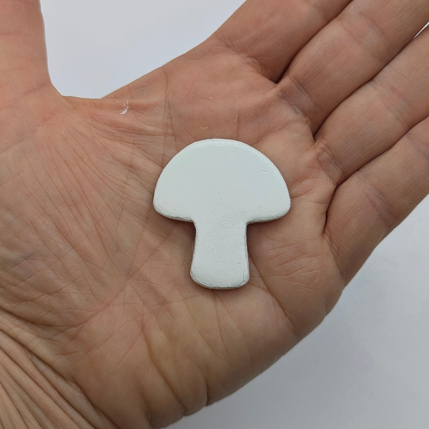 White mushroom shaped clay decoration held in a hand against a white background