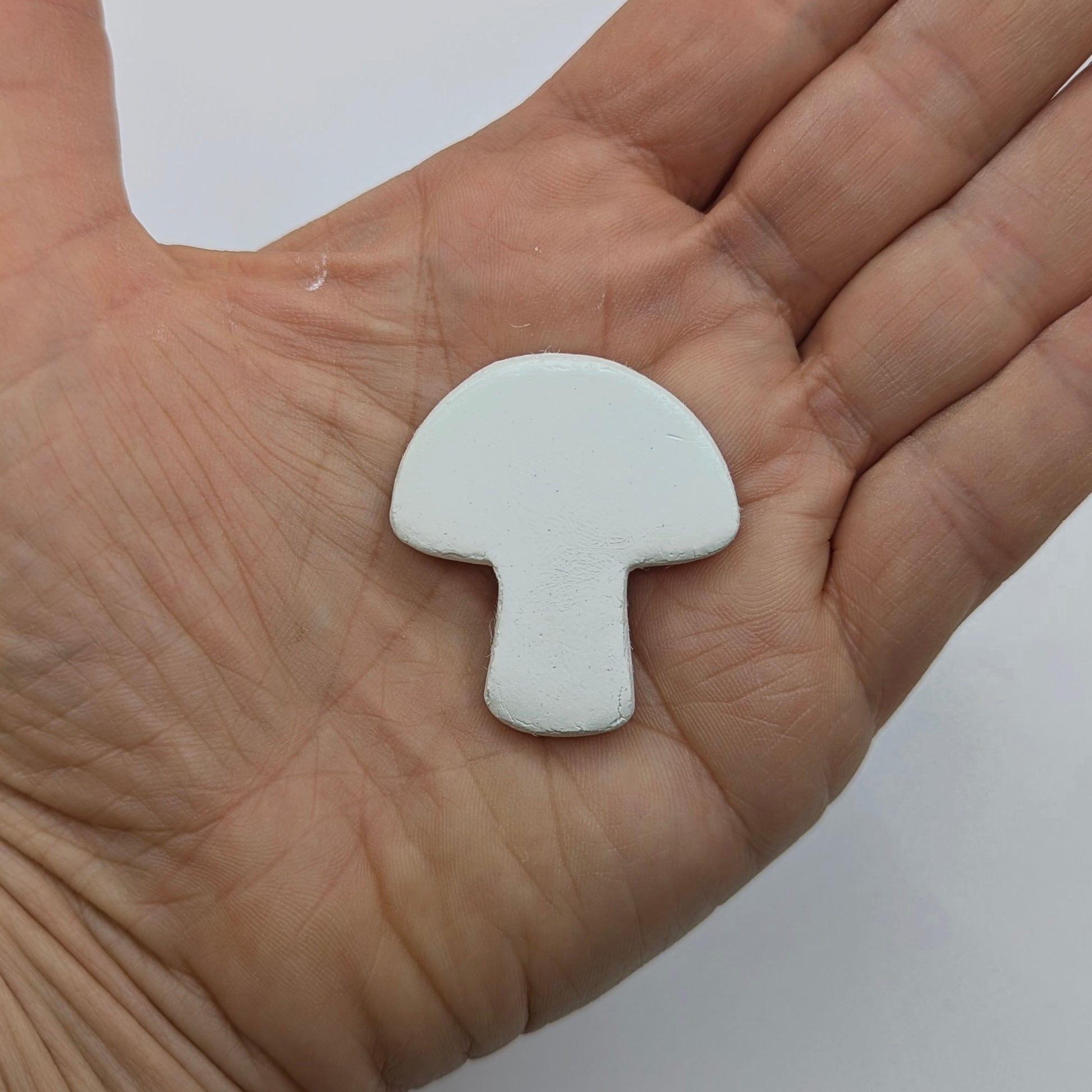 White mushroom shaped clay decoration held in a hand against a white background