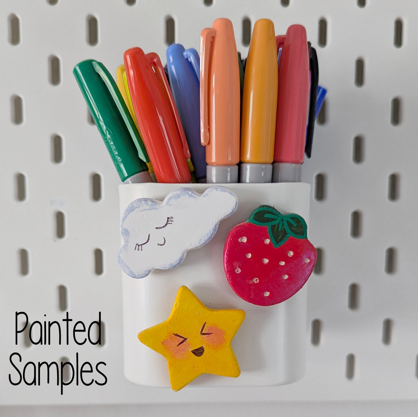 Colorful markers on a pegboard with min cloud,star and strawberry clay decoration with 'Painted Samples' text on