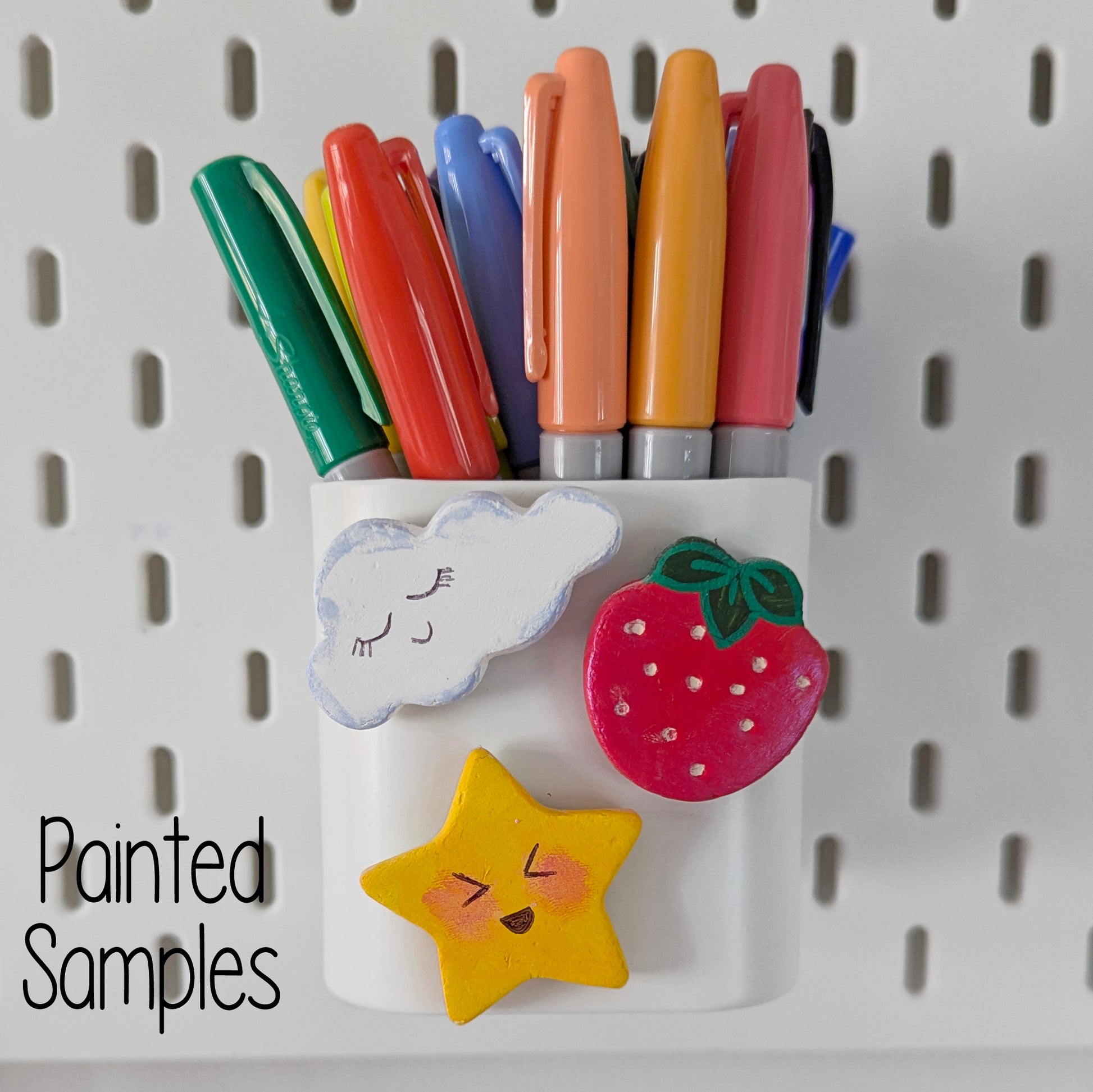 Colorful markers on a pegboard with min cloud,star and strawberry clay decoration with 'Painted Samples' text on