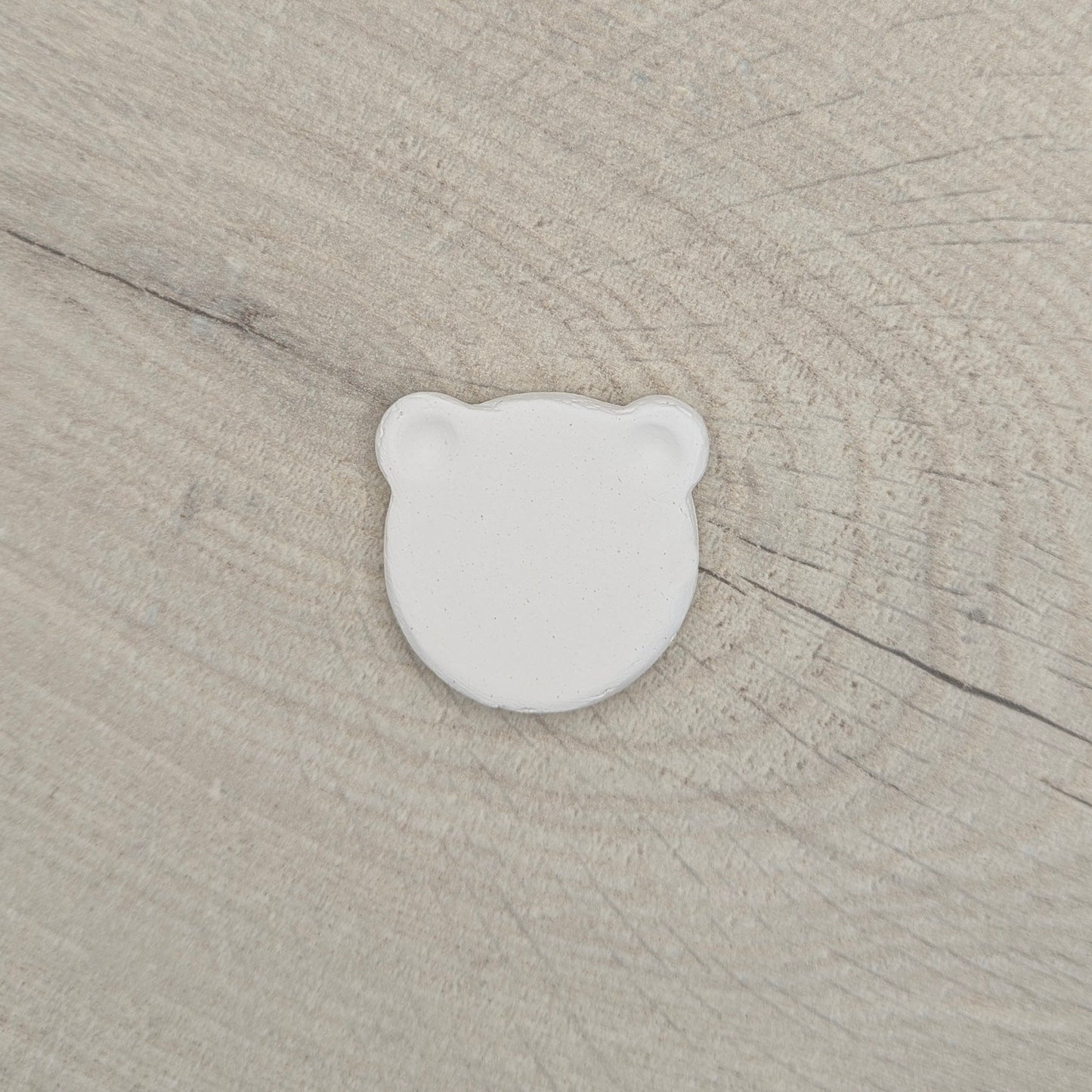 White air dried clay bear shaped decoration on a beige wooden surface