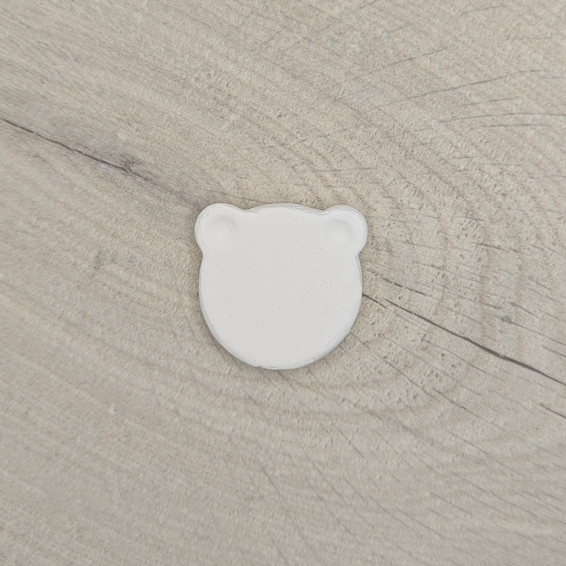 White air dried clay bear shaped decoration on a beige wooden surface