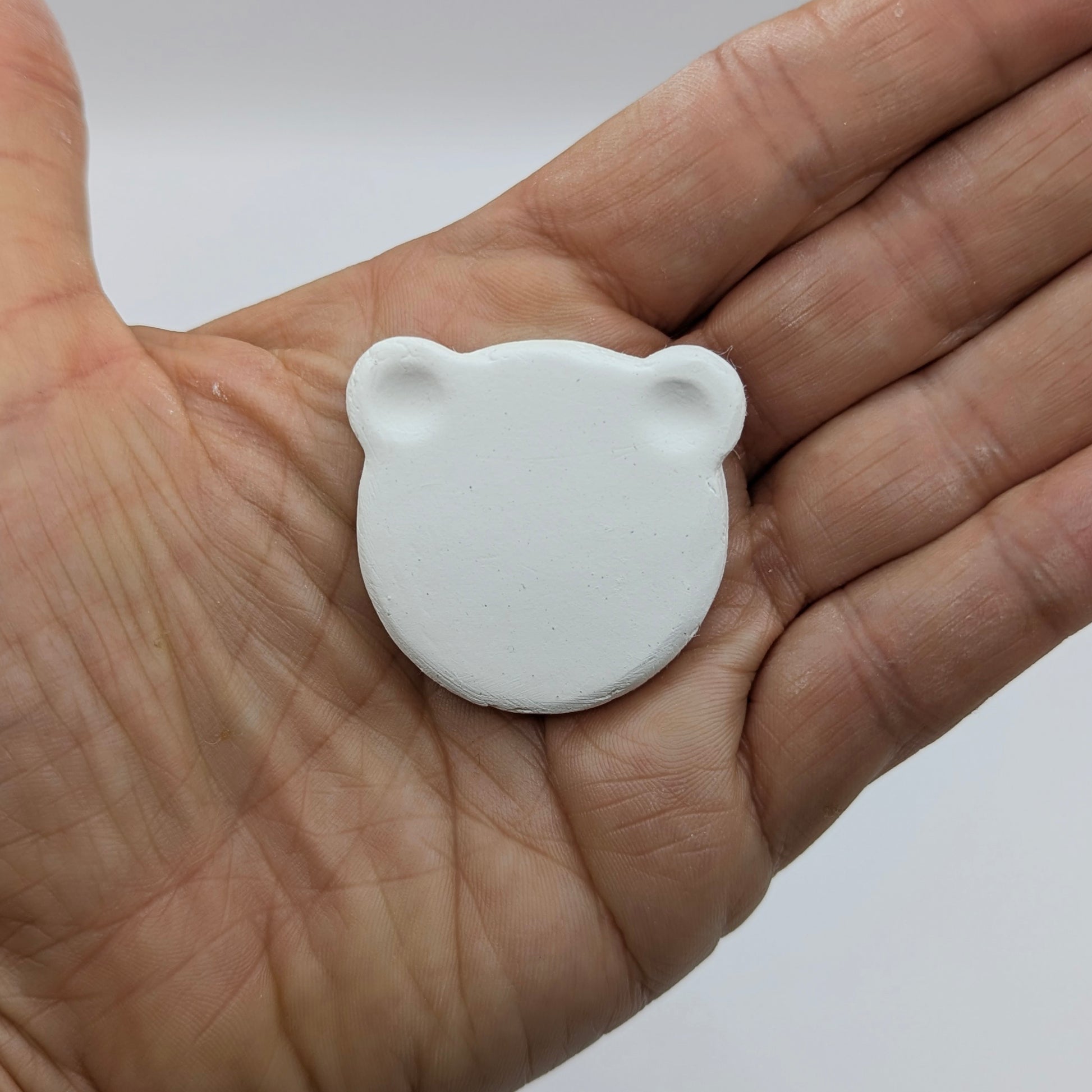 White air dried clay bear shaped decoration held in palm of hand to show scale