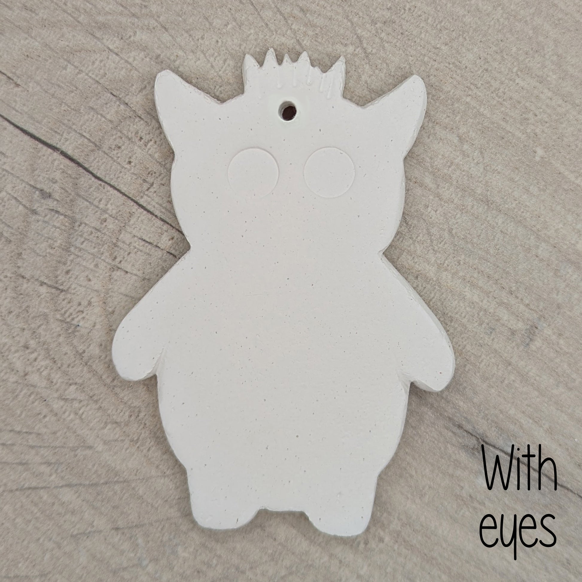 White silhouette of a funky monster with spikey hair, a pointy pair of ears, 2 large round eyes, on a wooden surface