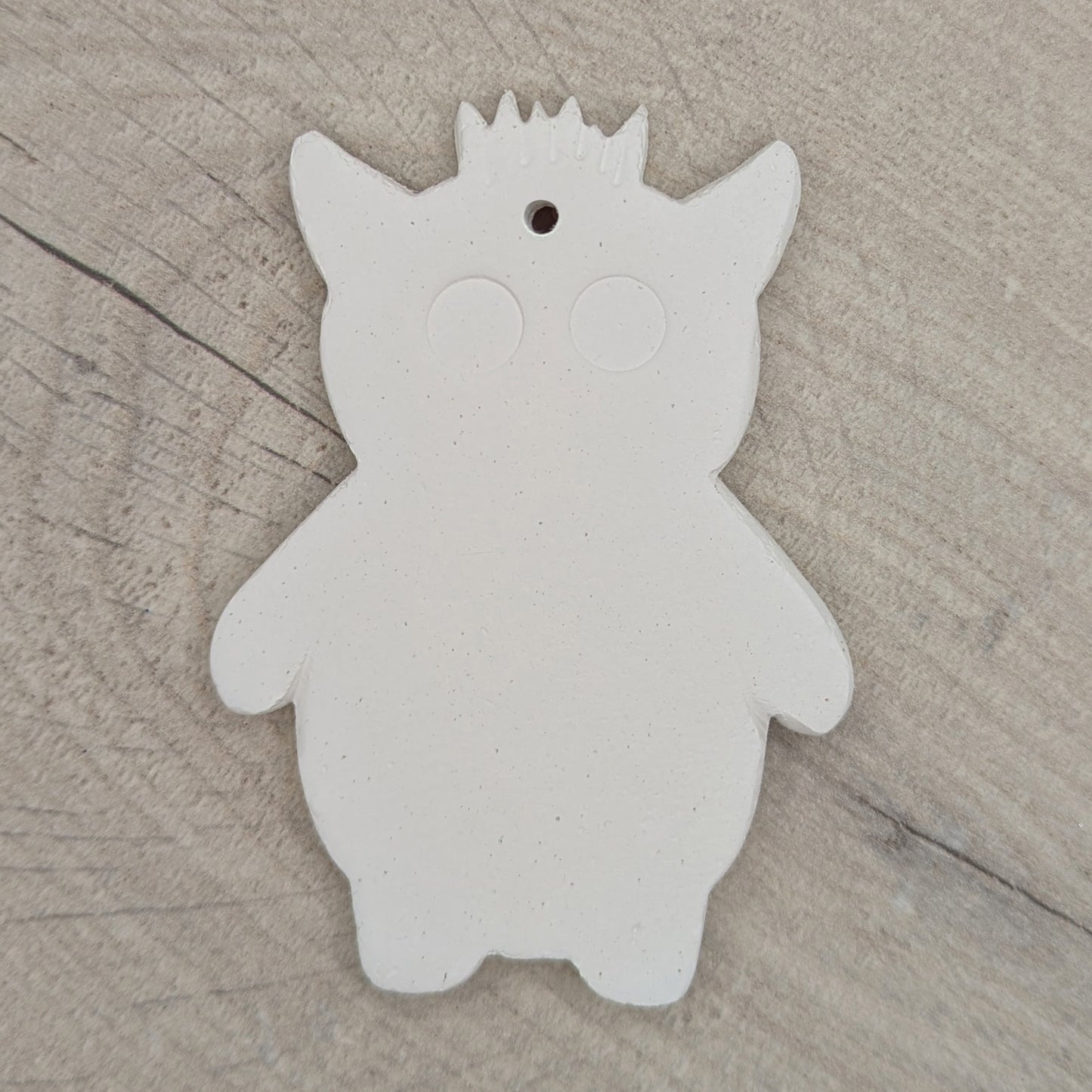 White silhouette of a funky monster with spikey hair, a pointy pair of ears, 2 large round eyes, on a wooden surface
