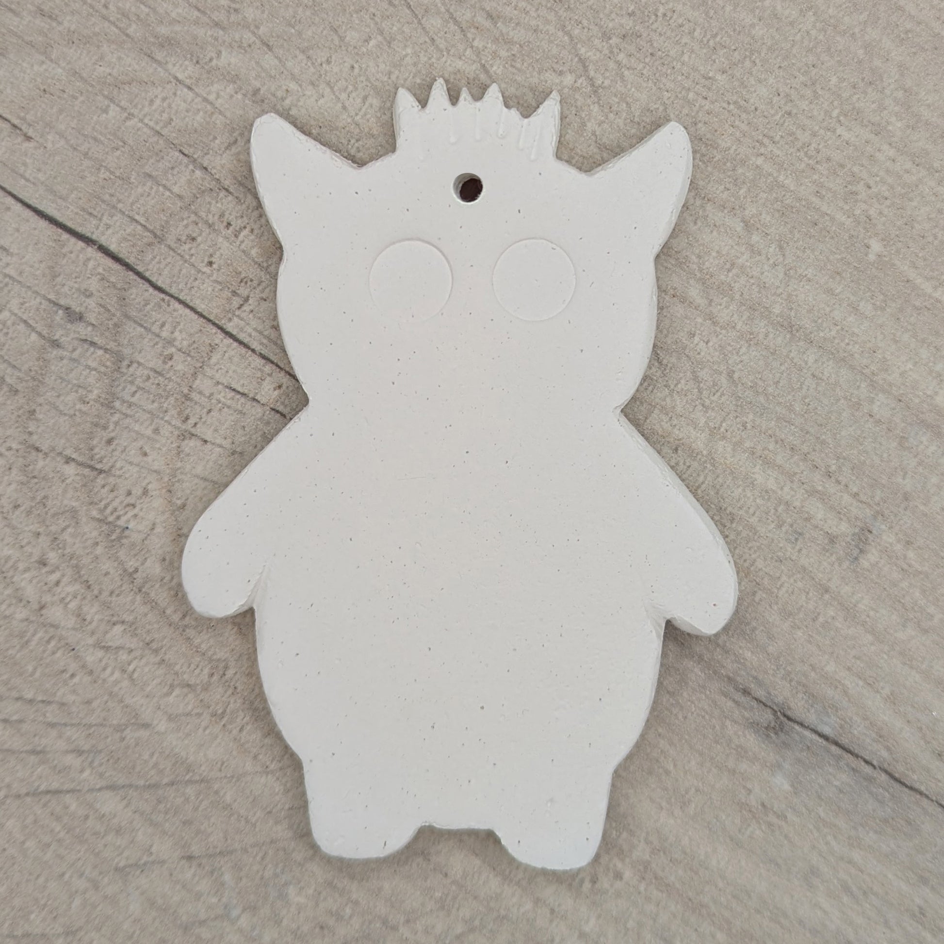 White silhouette of a funky monster with spikey hair, a pointy pair of ears, 2 large round eyes, on a wooden surface