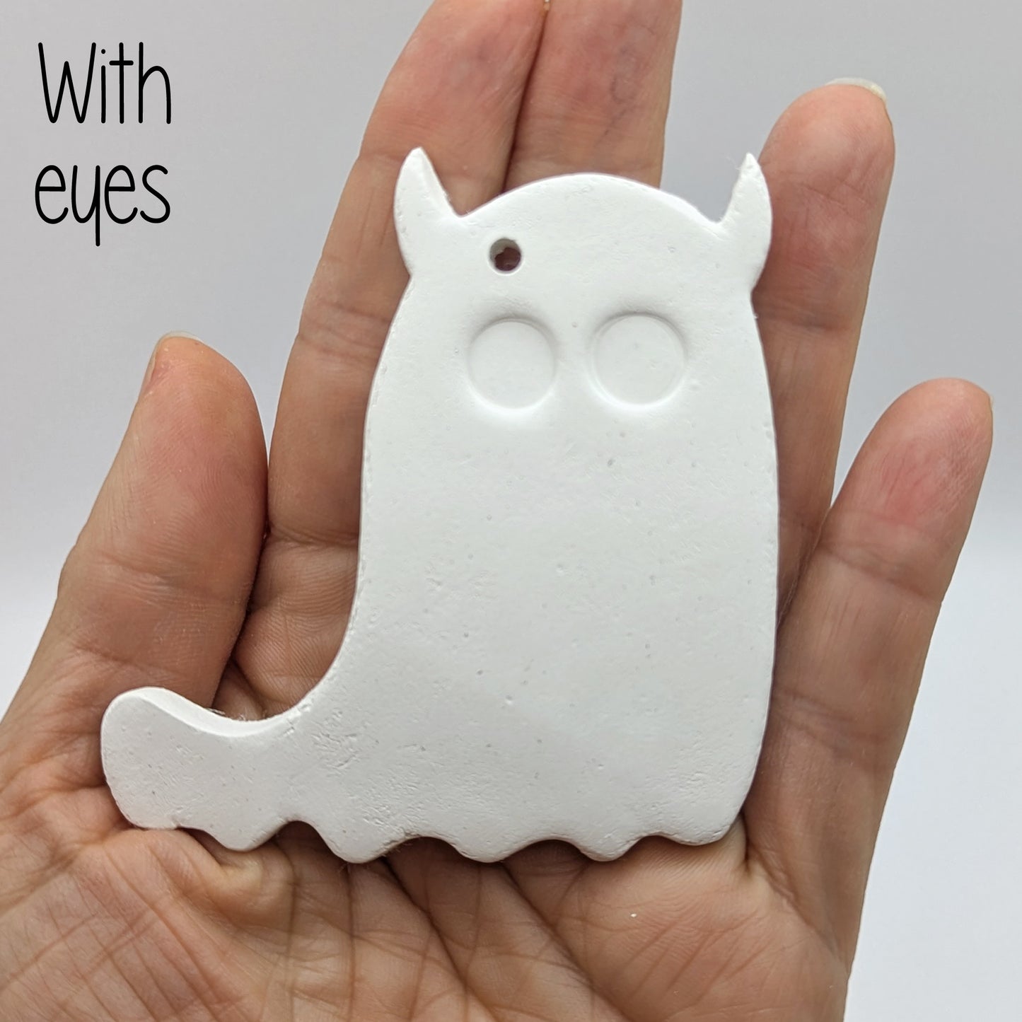 White ghost shaped air dried clay decoration - with eyes stamped in, held in a hand