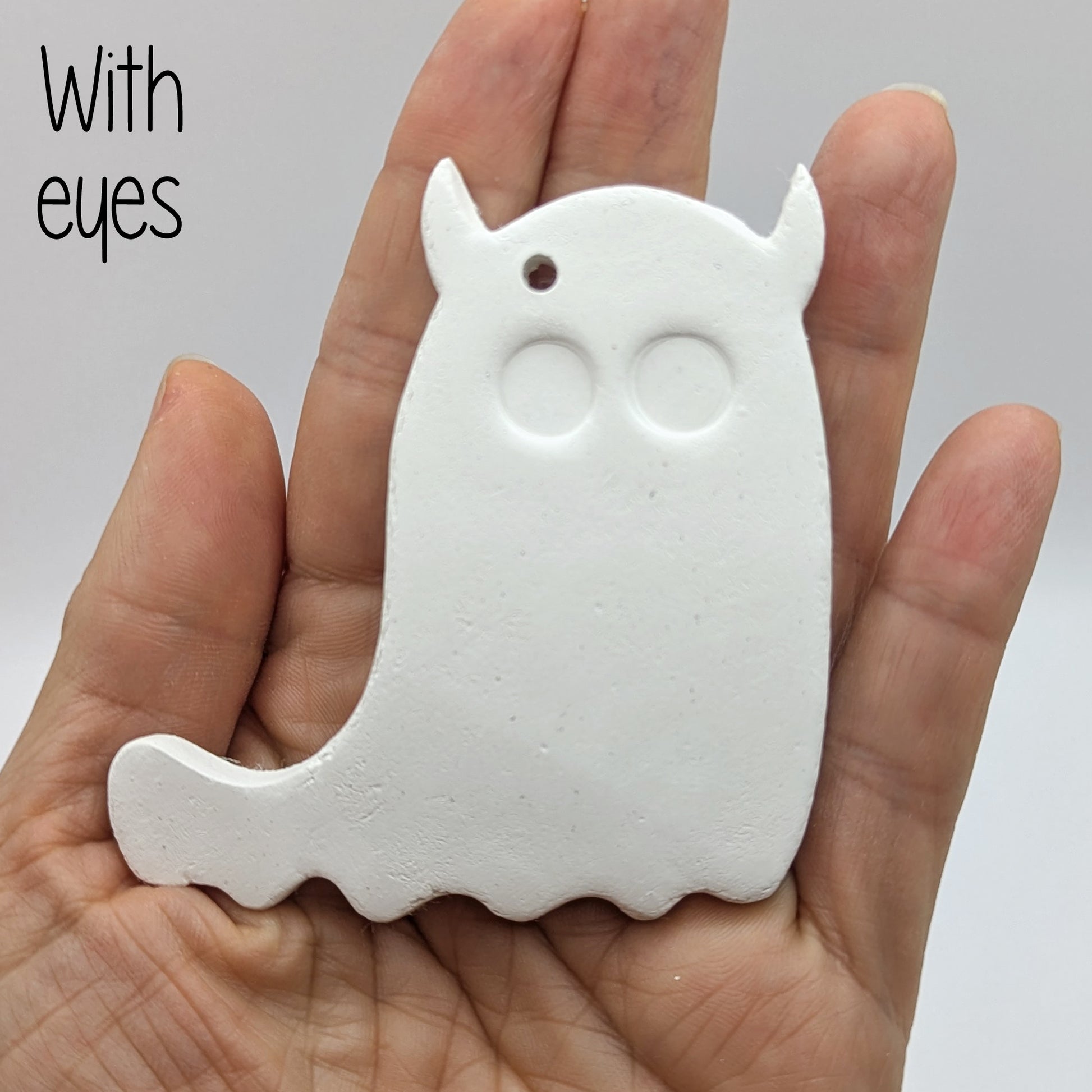 White ghost shaped air dried clay decoration - with eyes stamped in, held in a hand