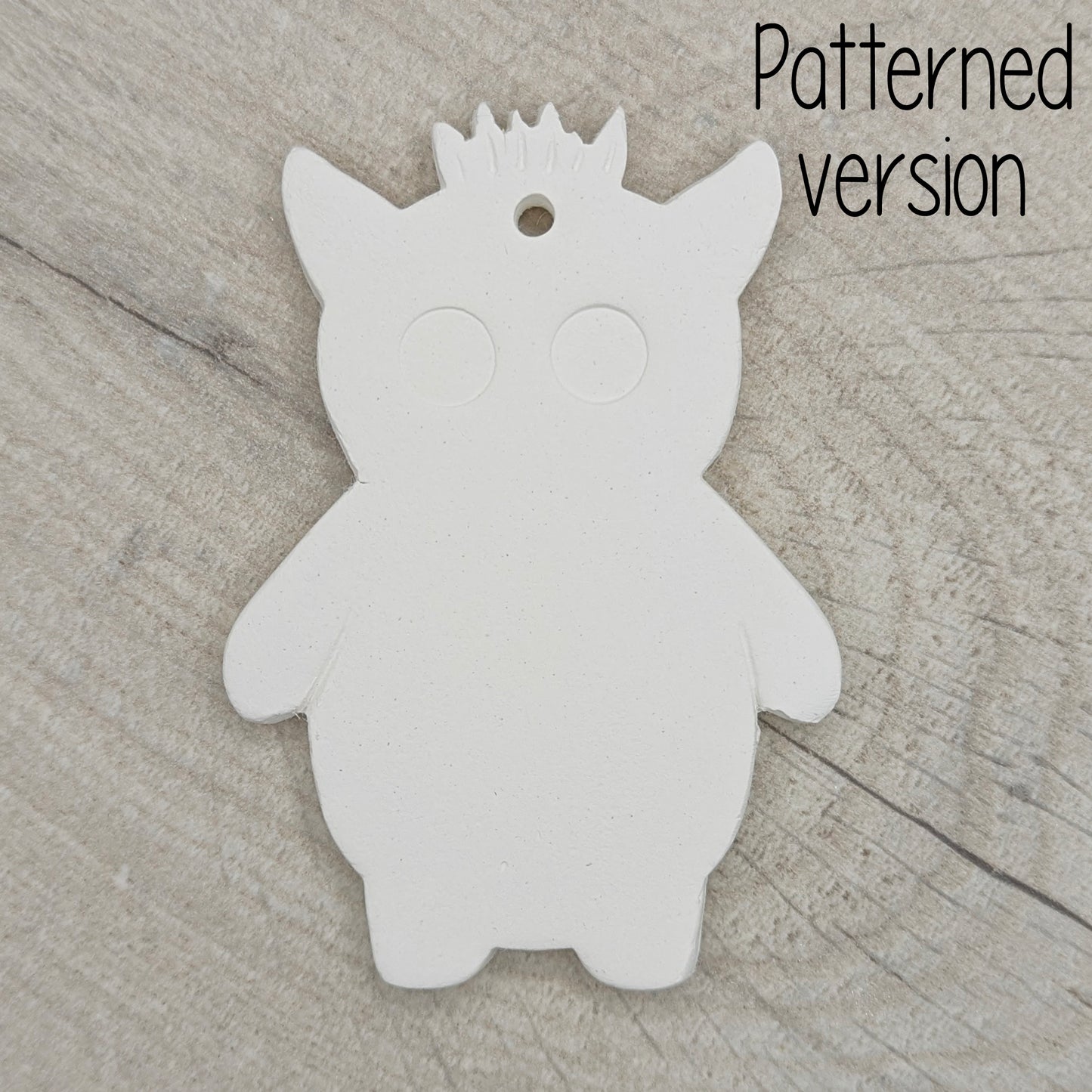 funky monster with spikey hair, a pointy pair of ears, 2 large round eyes, on a wooden surface