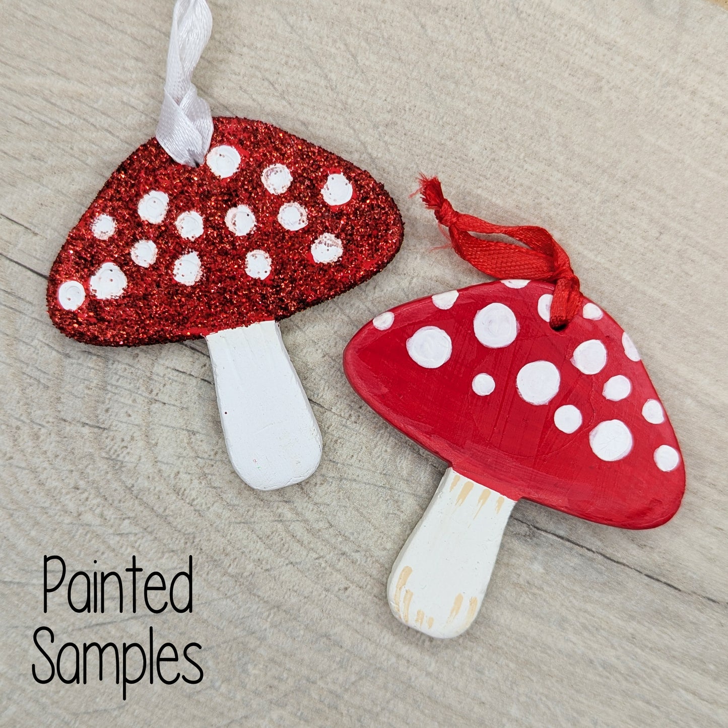 two clay mushrooms decorations, one painted in red with white spots the other with white paint for the spots and red glitter