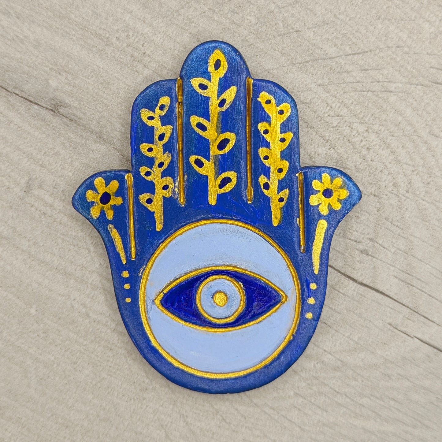 Decorative Hamsa hand with eye design on a wooden surface, painted in blue shades and gold 