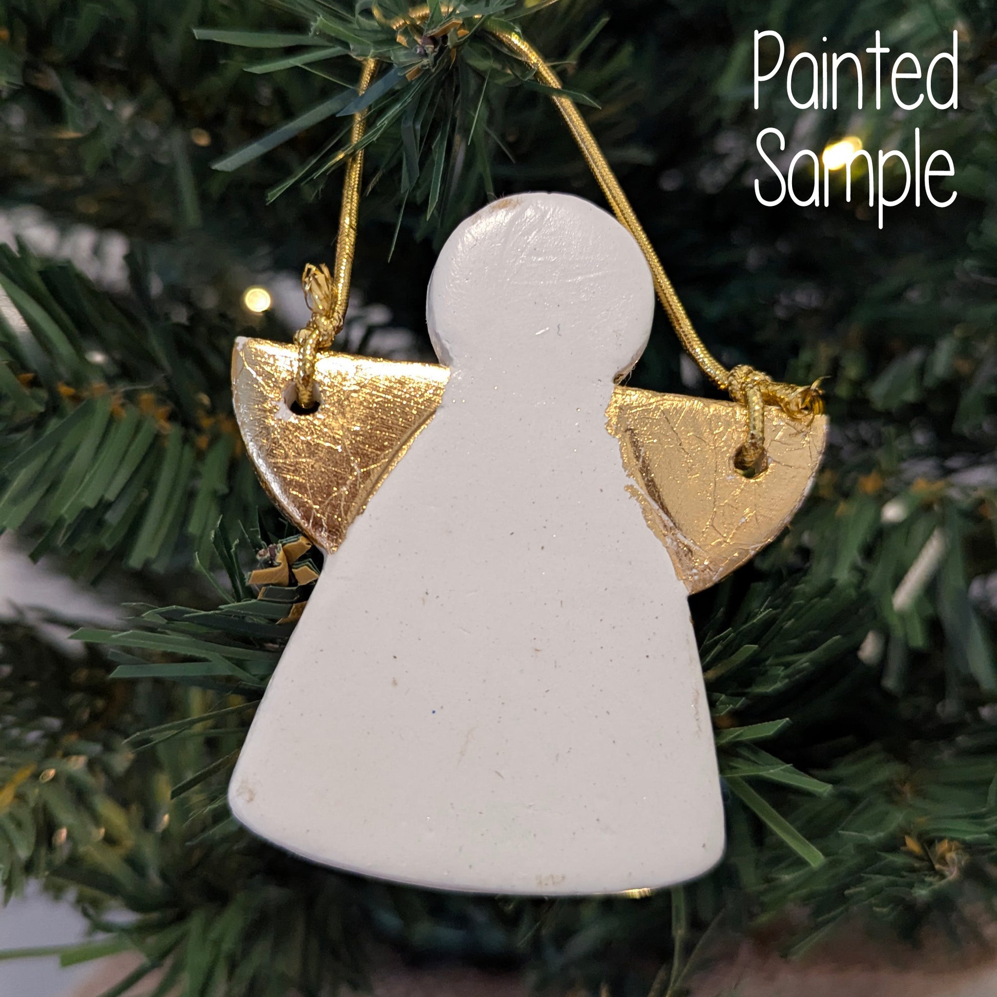 White angel shaped ornament with gold wings, hanging on a fake green Christmas tree.