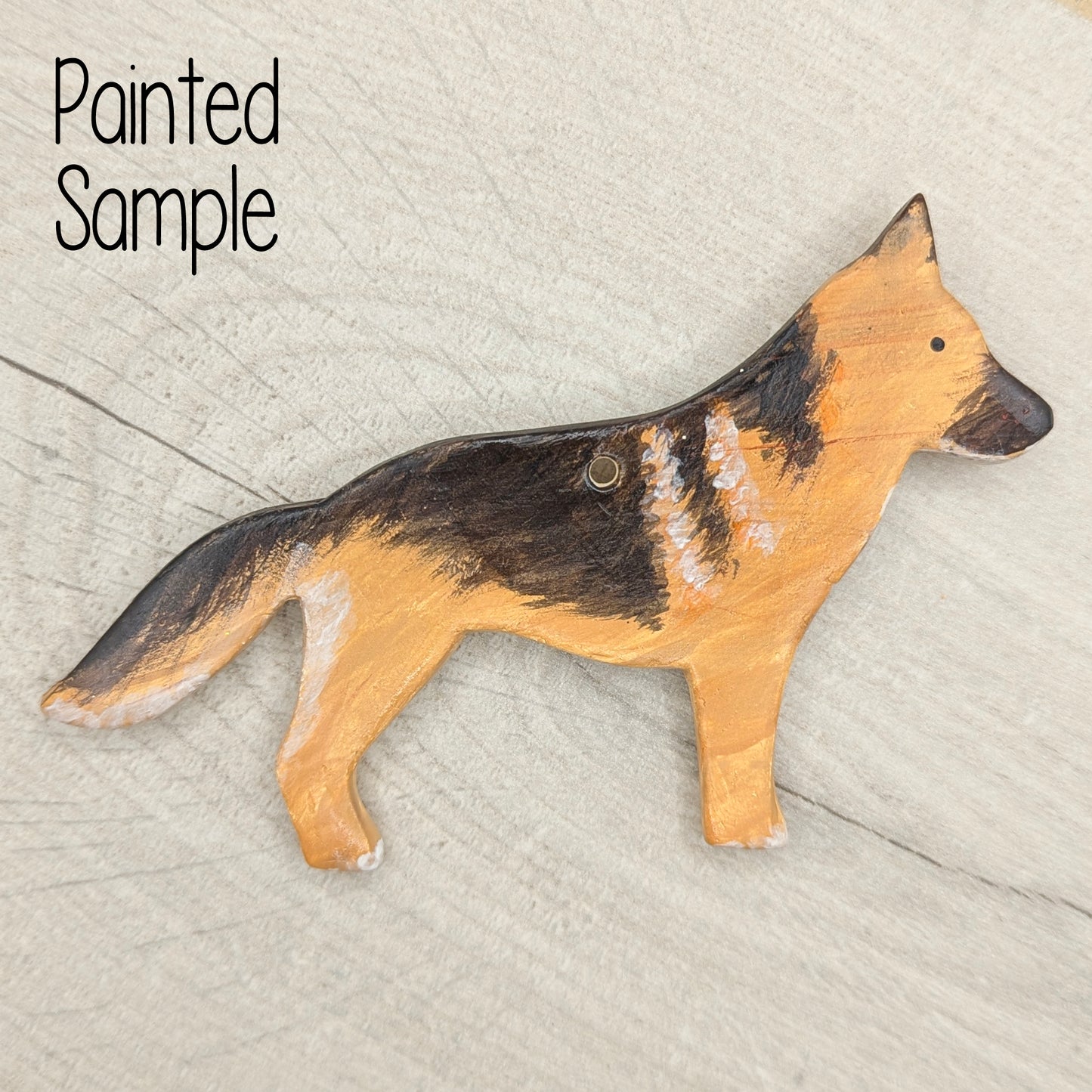 Painted black and tan clay decoration in the shape of a german shepherd, displayed on a light wood backround