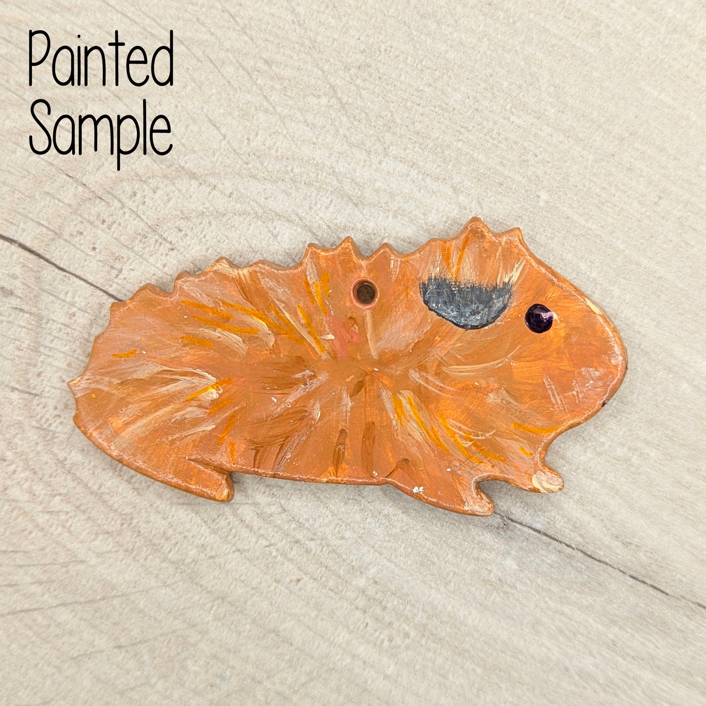 painted guinea pig decoration in beige brown colour with a black eye, shown on a wooden background