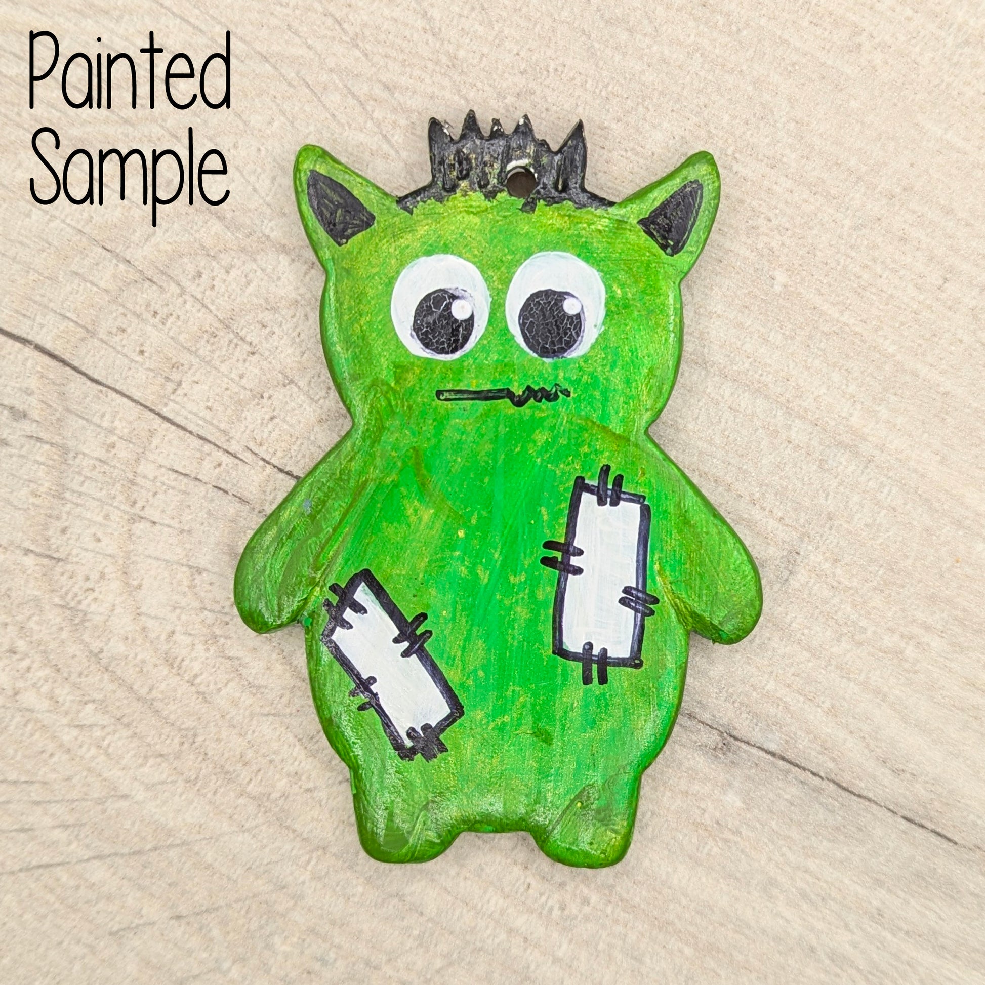 clay decoration painted in a bright green with black hair and plasters stuck on him, displayed on a wooden background