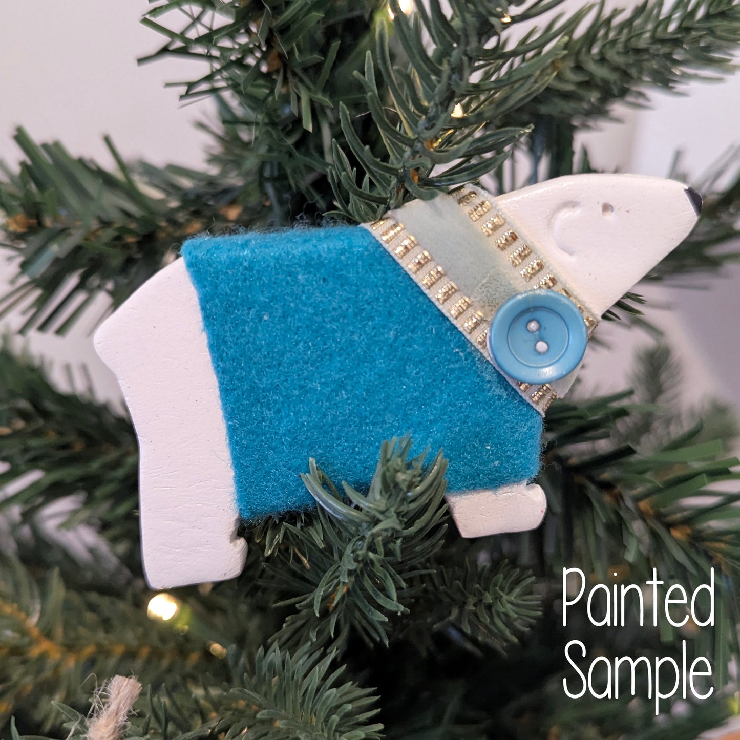 Decorative ornament of apolar bear wearing a blue felt sweater on a Christmas tree.