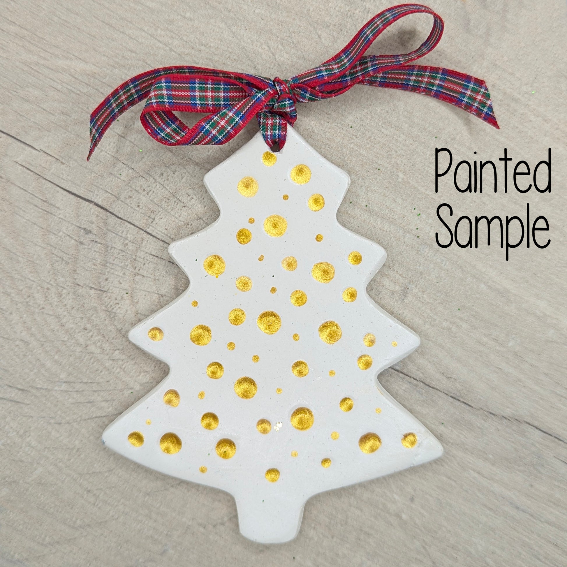 White clay Christmas tree decoration with gold dots and a red tartan ribbon on the top, displayed on a wooden surface