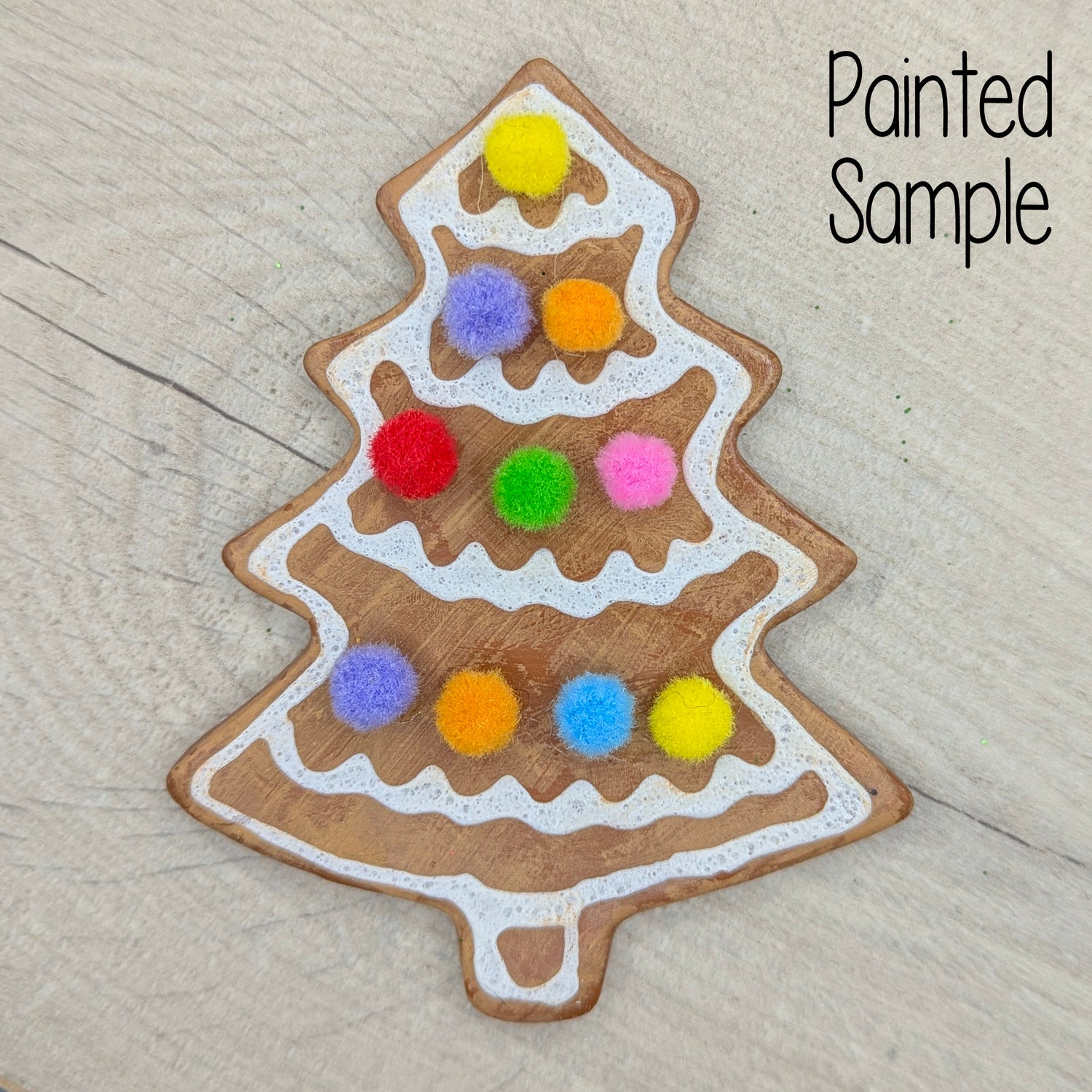 Gingerbread inspired Christmas tree decoration, with white puff paint and mini coloured pom pom details, on a wooden surface