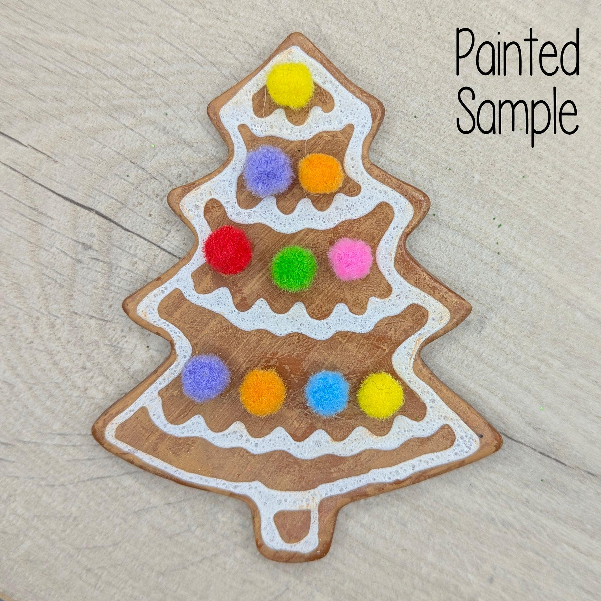 Gingerbread inspired Christmas tree decoration, with white puff paint and mini coloured pom pom details, on a wooden surface